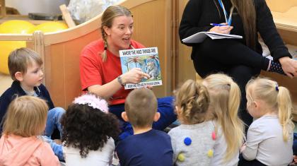 A woman in a red T-shirt reads to a group of children Where The Wild Things Are