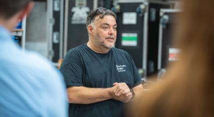 Centred in the frame the Northern Ballet Technical Director, out of focus to the left and right of the image, two people looking at and listening to the Director