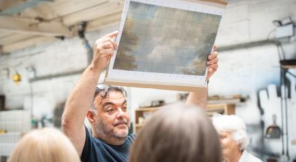 The Northern Ballet Technical Director holding an image of a cloudy sky above his head to gathered donors, it will be painted on a large scale to become a backdrop for a production