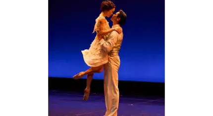 A man lifts a woman by the waise, she looks down at him as their faces almost touch lovingly