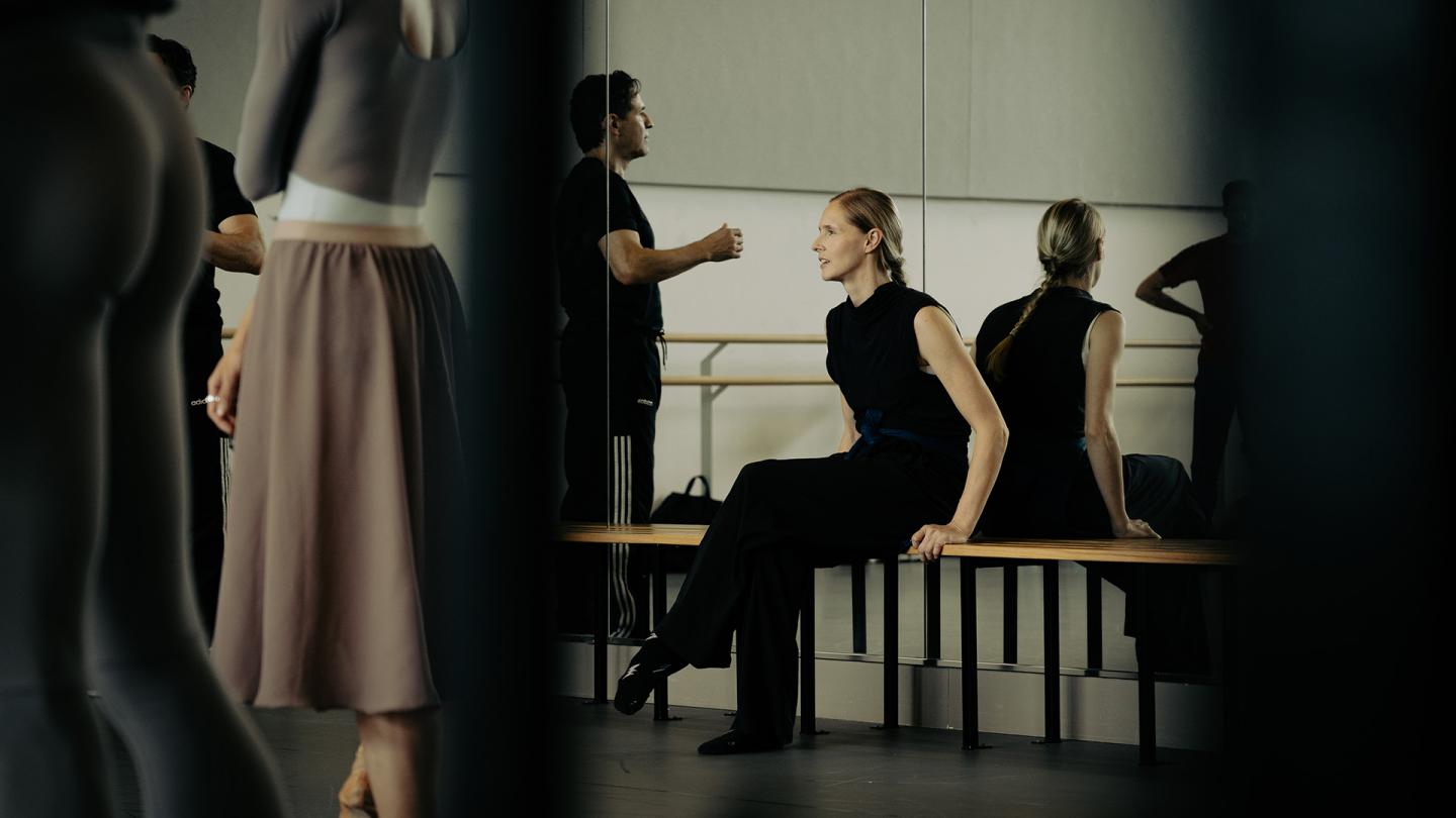 Choreographer Sina Quagebeur, wearing black and sat overseeing a rehearsal session