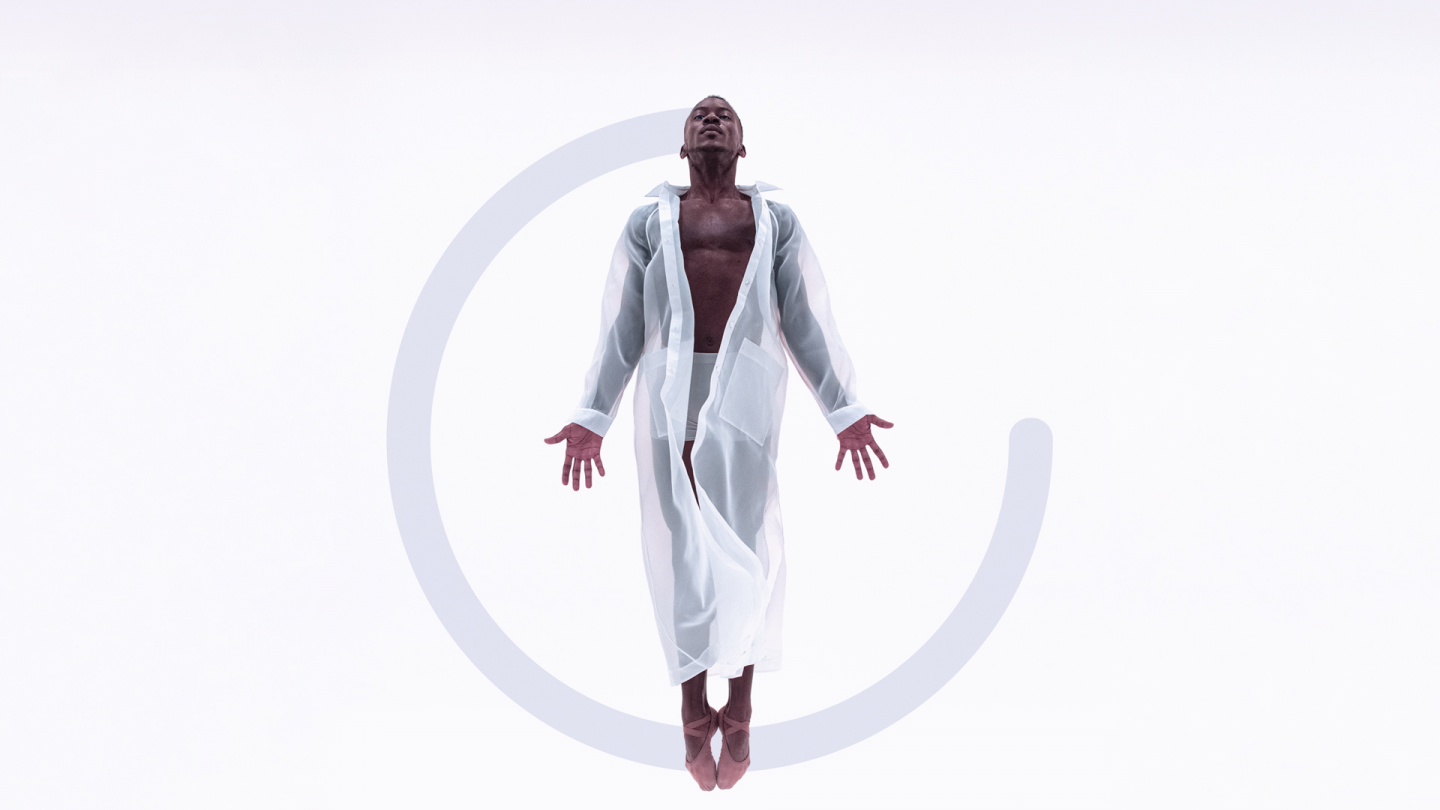 A man is floating in the air wearing a sheer white jacket, which is long sleeve and goes down to their ankles. The are looking up towards the sky with their palms faced to the front. There is a grey semi-cirle graphic added to the image behind the dancer. 