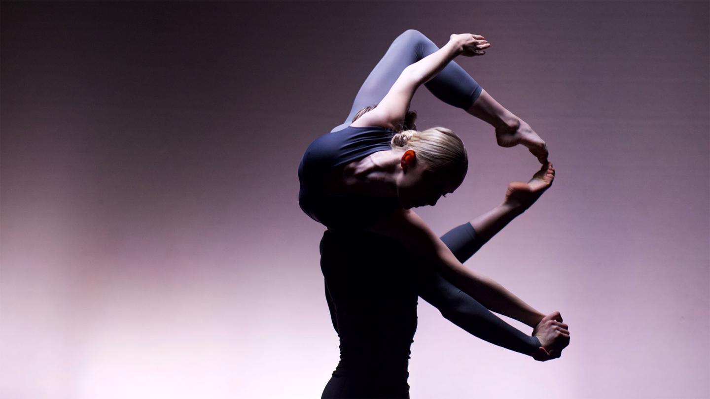 Against a lilac-coloured backdrop one dancer lifts another on his shoulders