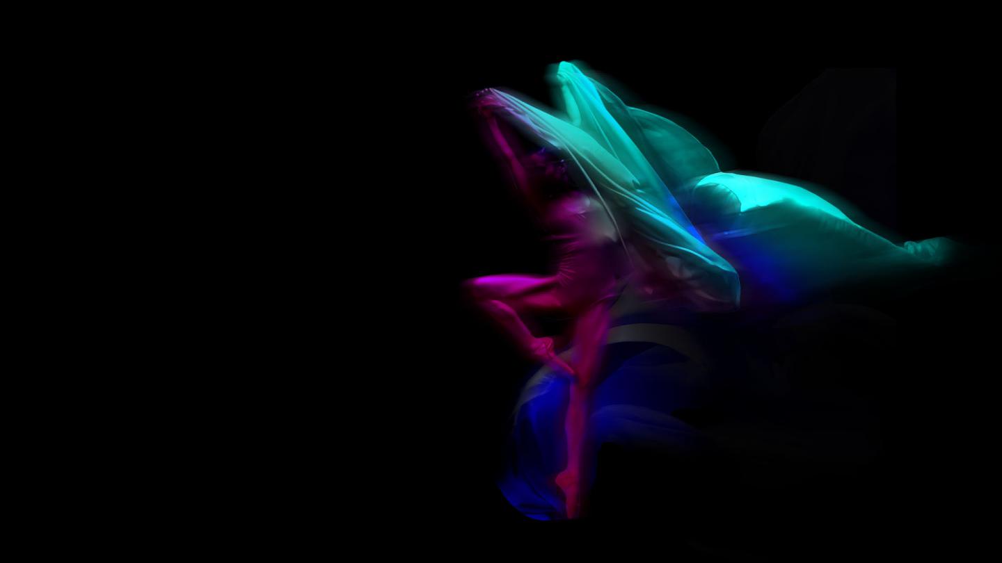 Stylized image of a dancer against a black background lit in magenta and cyan, slightly blurred with motion