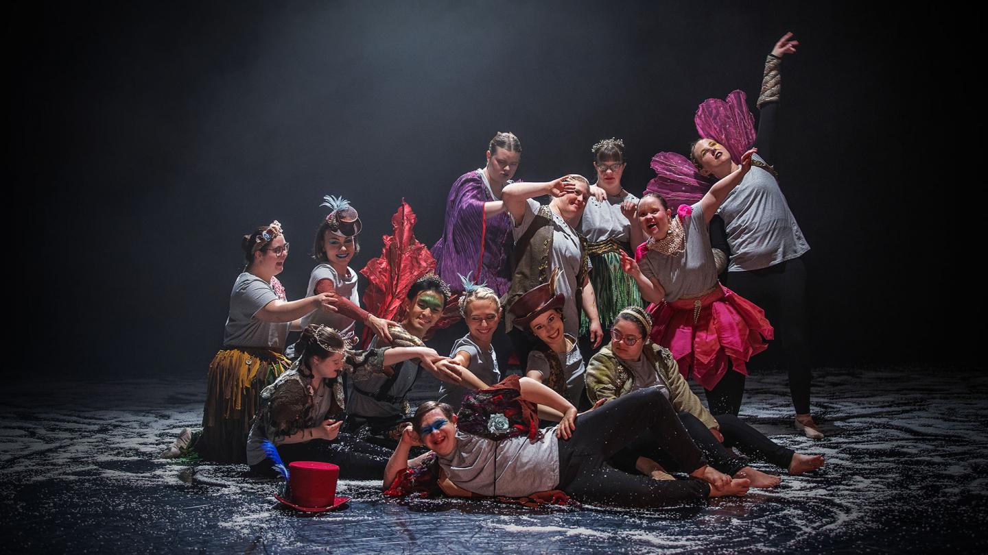 Dancers posing for a poster image dressed in their costumes of grey T-shirts jazzed-up with feather boas, wings, colourful waistcoats, hats and more