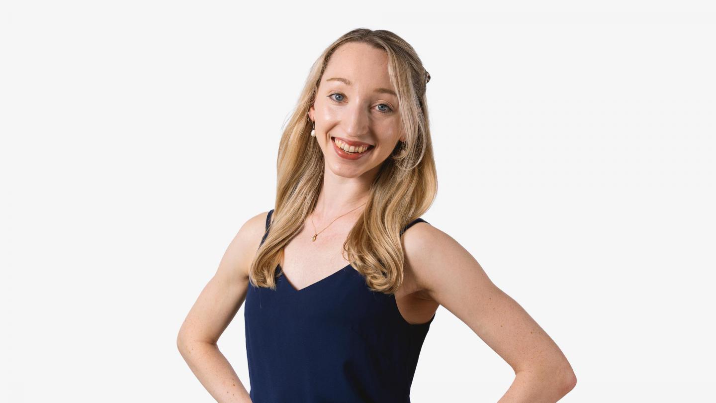 A headshot of a woman looking forward with blonde hair and a navy top