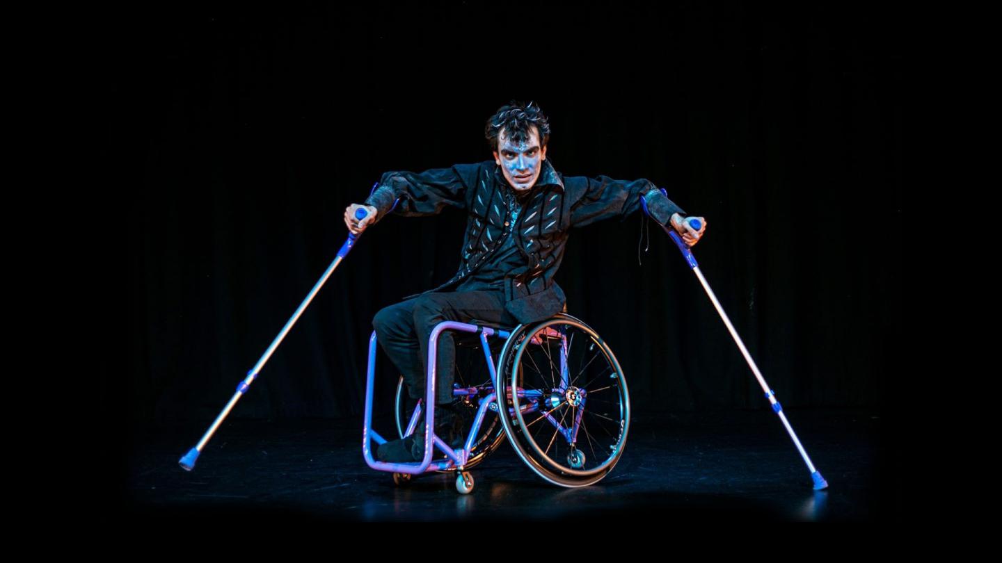 Man in a wheelchair against a black stage looking intently at the camera