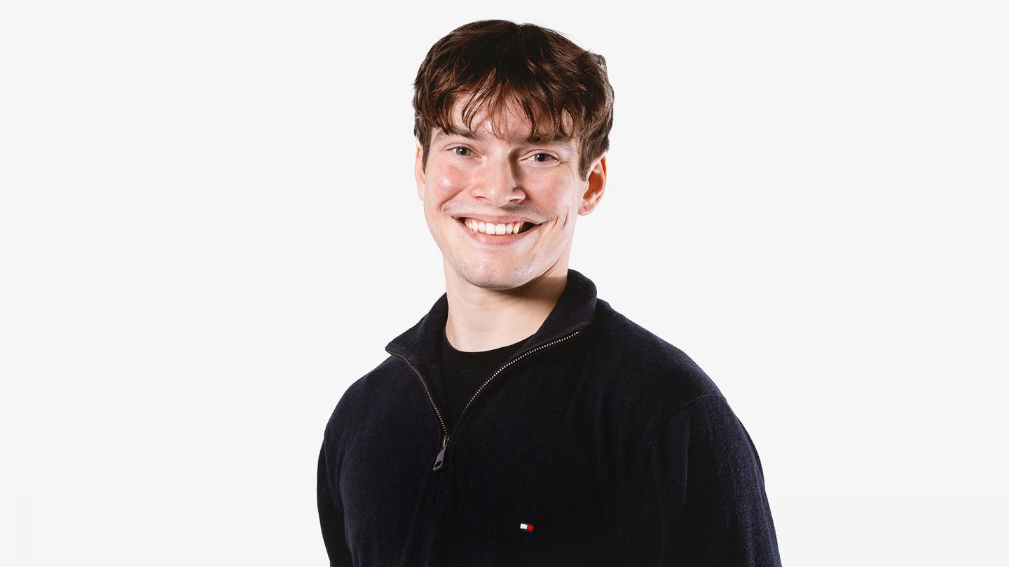 Wearing a black fleece jacket, a man smiles broadly at the camera, he has short brown hair