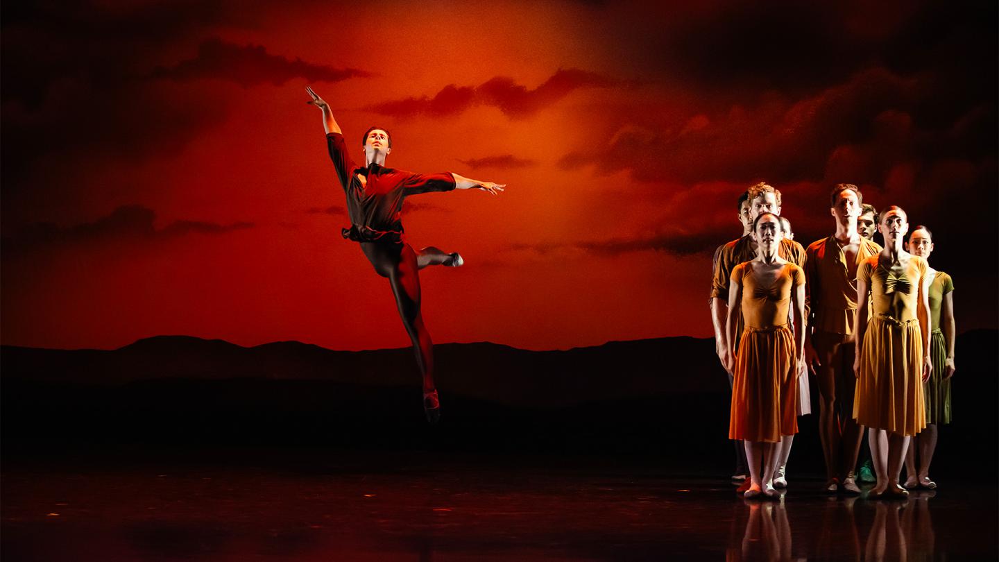Dressed in red, a dancer leaps high against an orange sunset