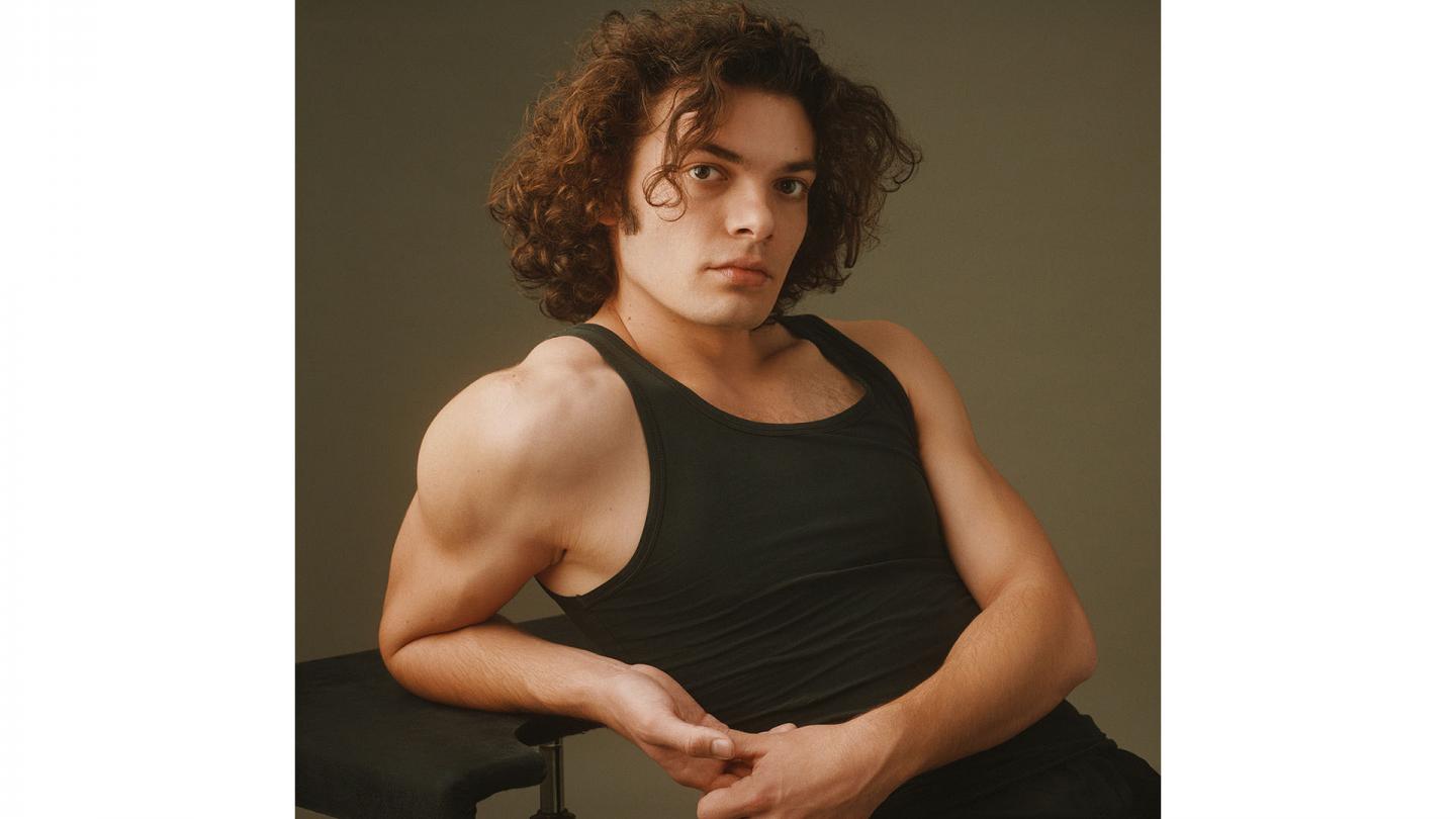 Man in black vest with medium length, curly hair looking intently at the camera