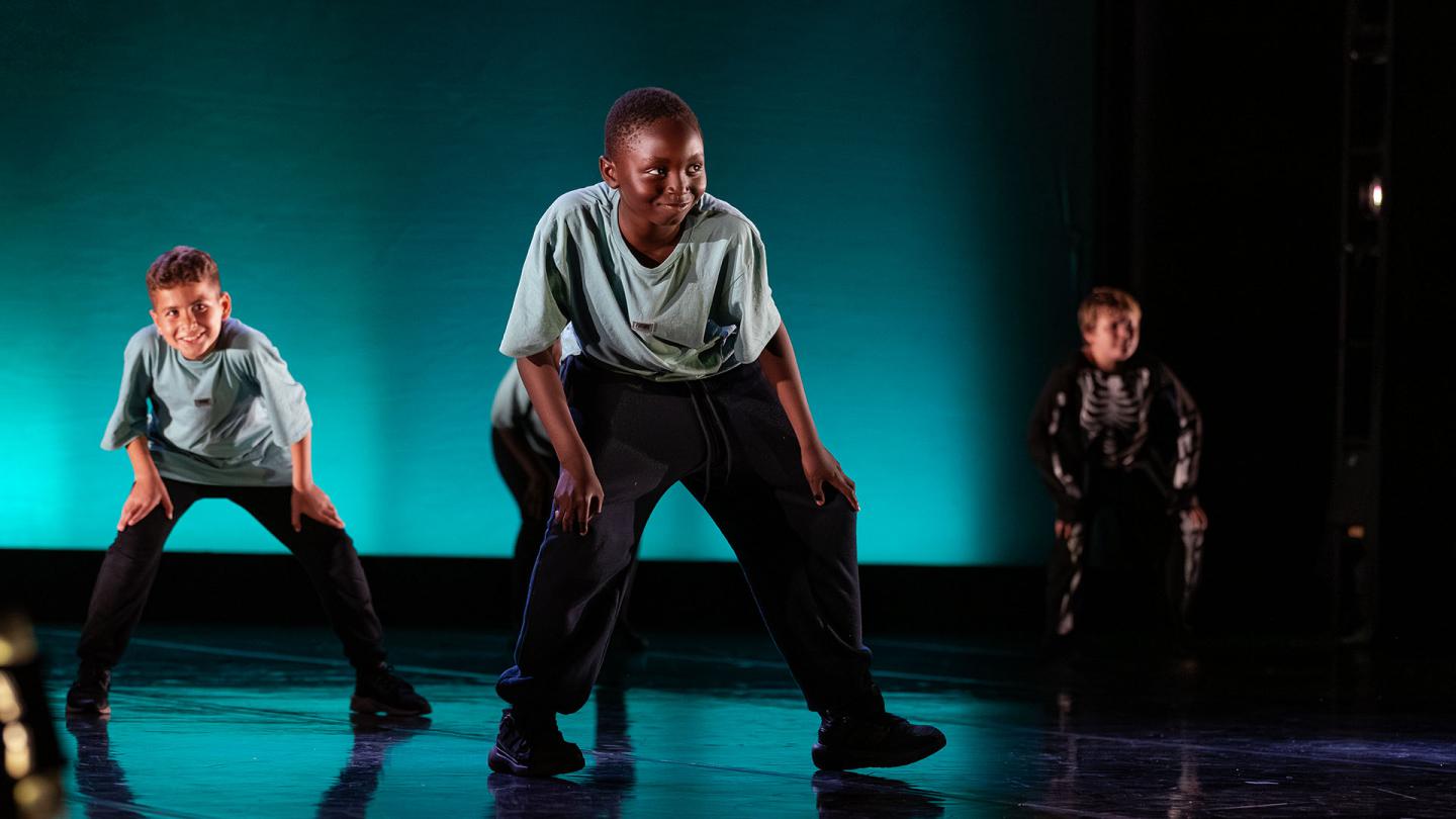 Young people dancing on a black stage against a blue-lit background