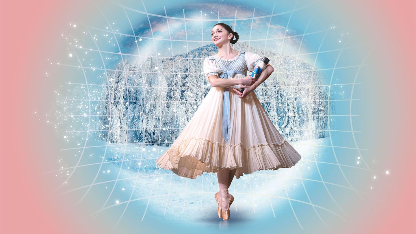 A dancer in Edwardian costume hold a Nutcracker doll in her arms, stands en pointe and smiles with childlike wonder