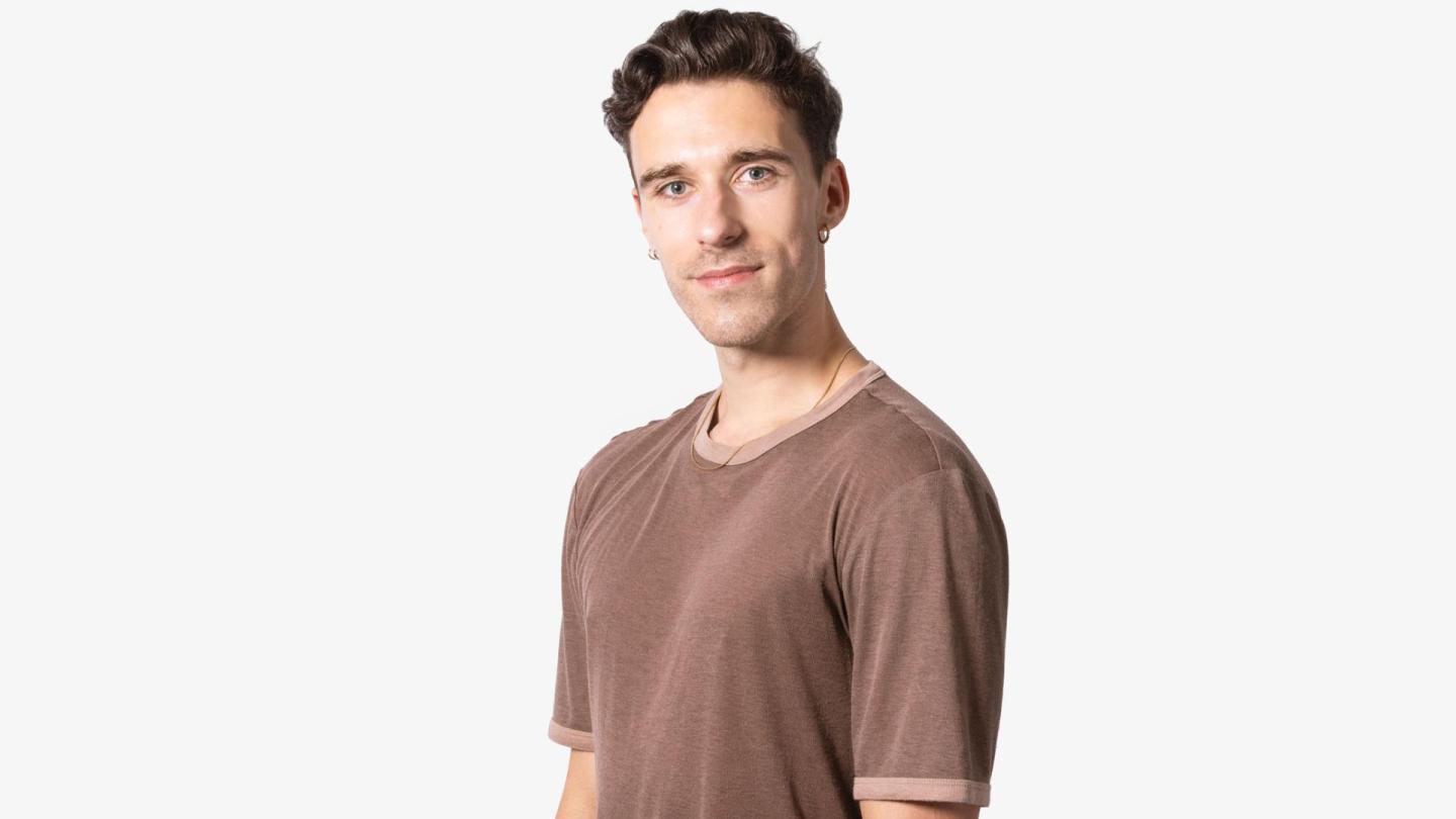 A headshot of a man with dark hair in a brown tshirt