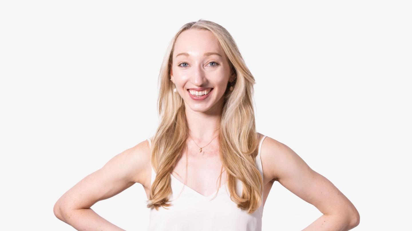A headshot of a woman with blonde hair stood facing the camera in a white top.
