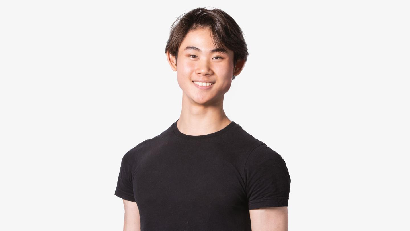 A man with short brown hair stood on a white background wearing a black t-shirt.