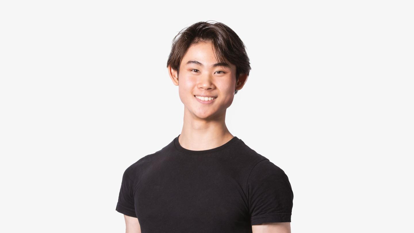 A man with short brown hair stood on a white background wearing a black t-shirt.