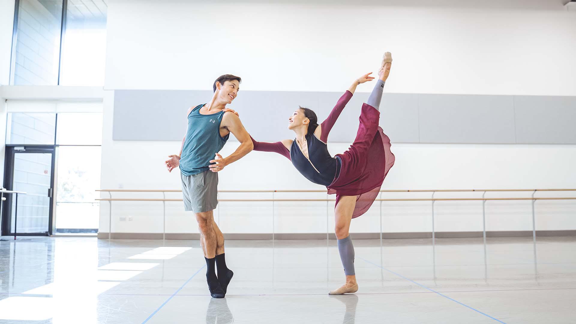 A female dancer is in full arabesque with her leg hyper extended while she holds on to another dancer who is on his toes