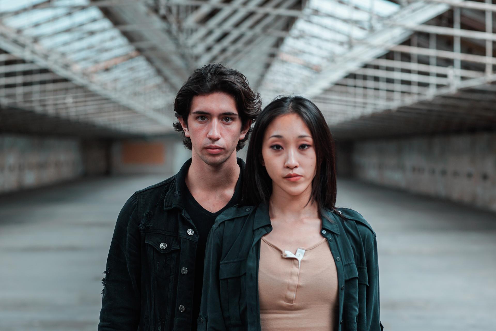 A man and a woman stand in a warehouse staring directly into camera
