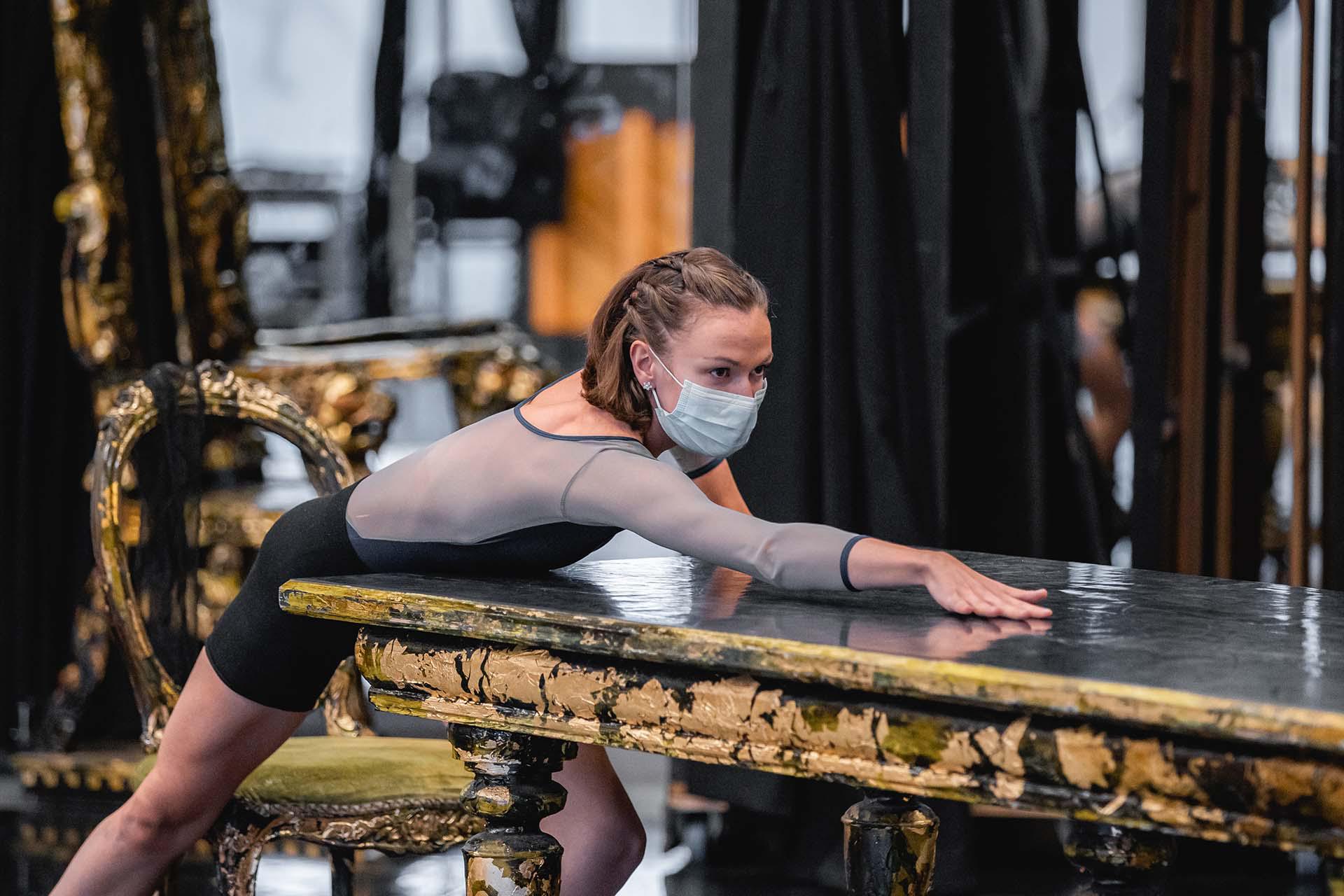 Abigail Prudames rehearing the role of MM leaning forward over a table looking suggestively at whoever is at the other end of the table which we cannot see