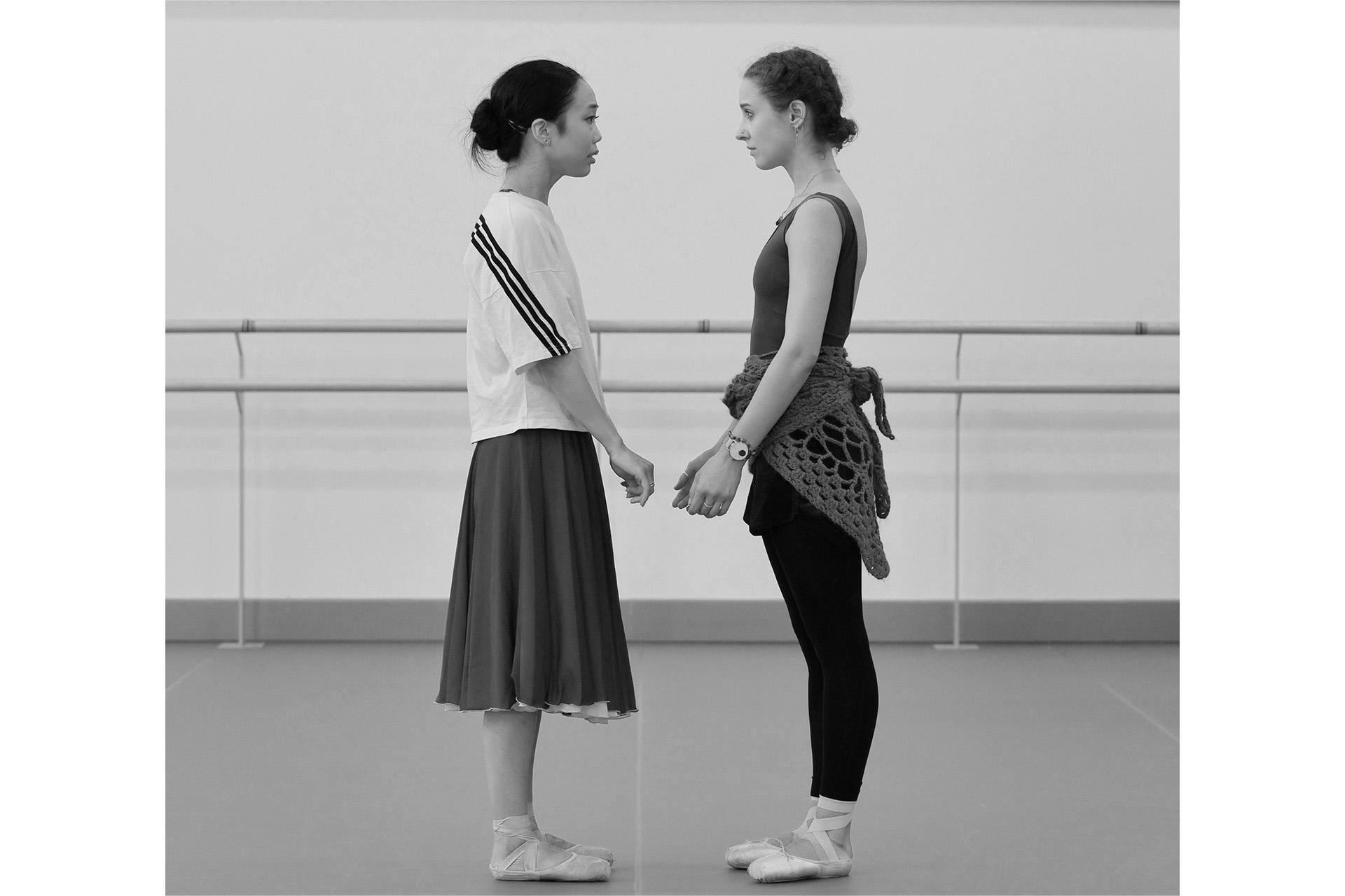 Black and white photo of dancers in rehearsal clothes looking at each other with familial love