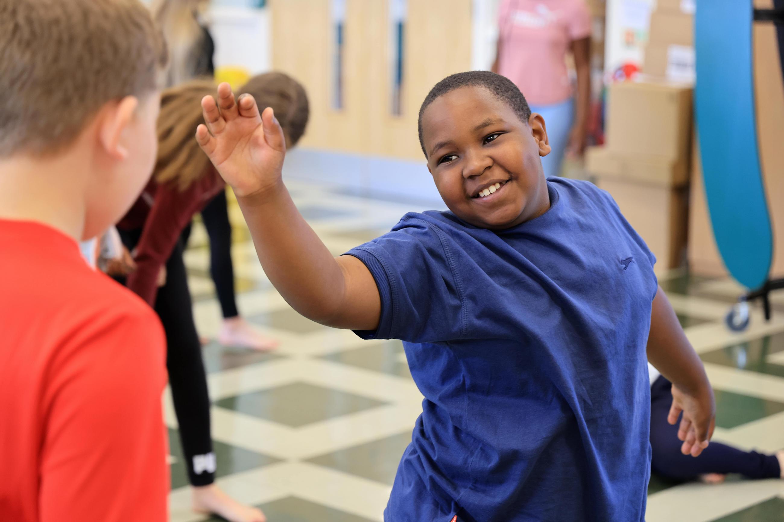 A boy in a purple t-shirt smile whilst dancing.