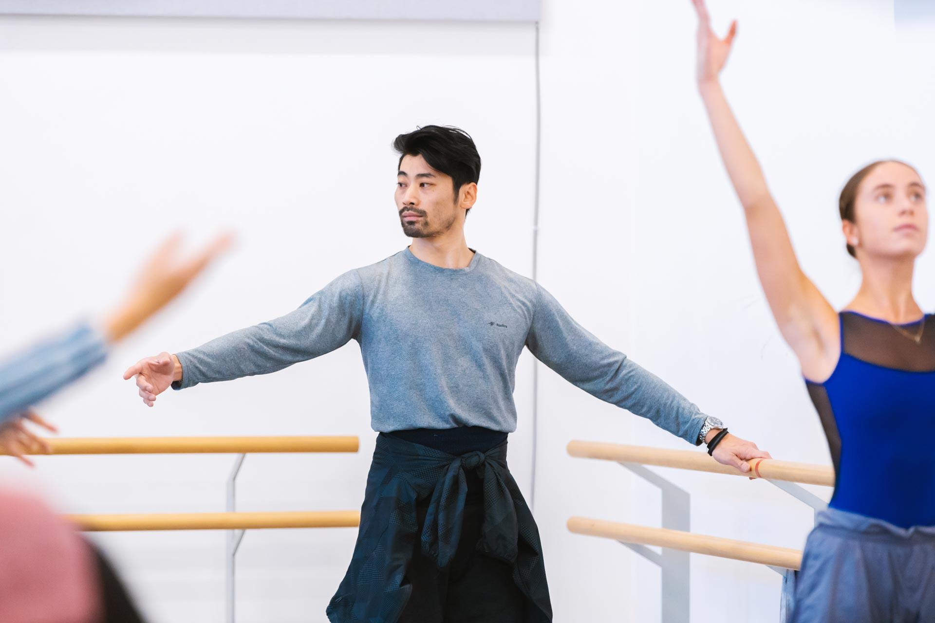 Male dancer in ballet class with arms raised, one arm on the barre