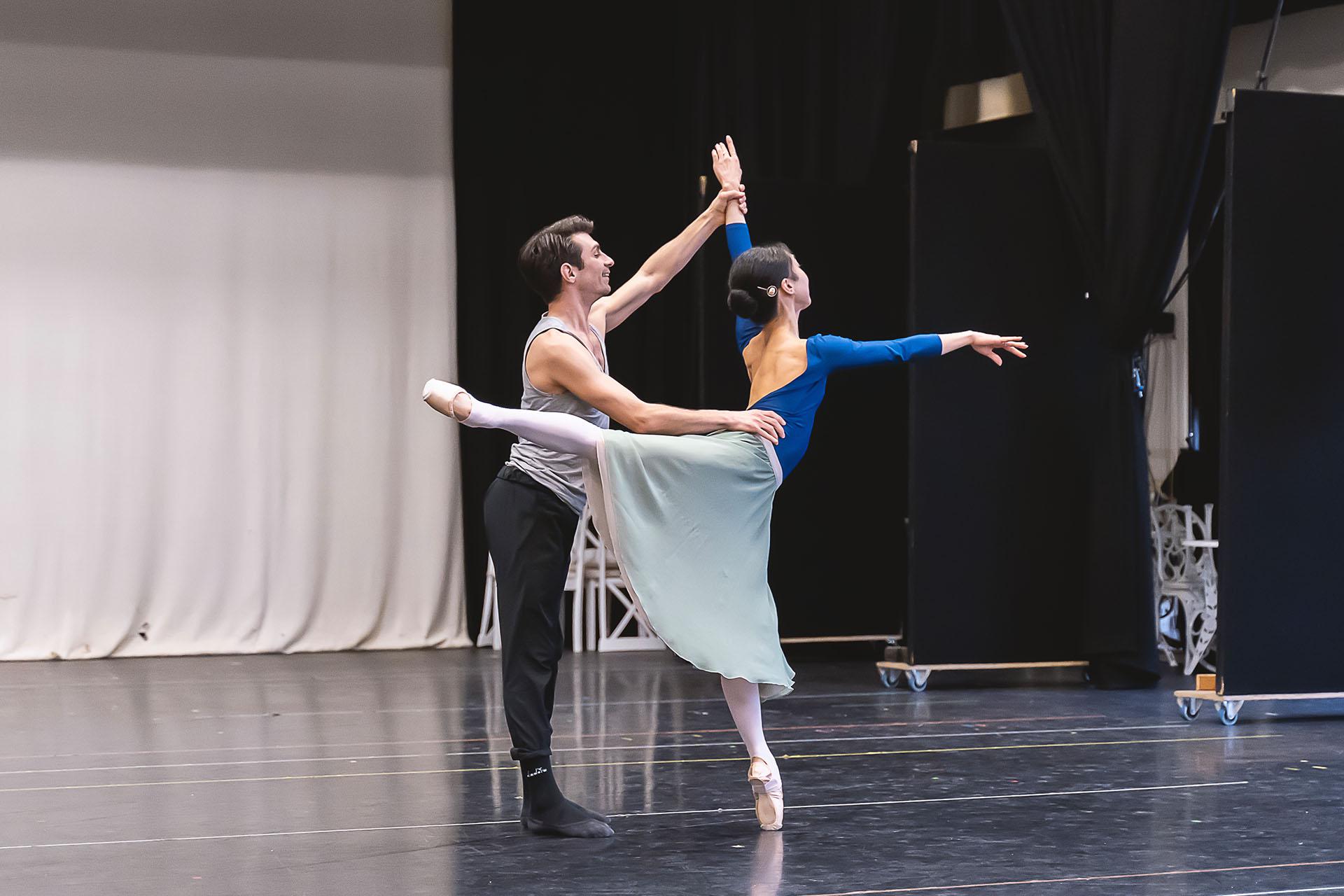 Dancer stood arabesque while supported by her raised arm and her waist by another dancer