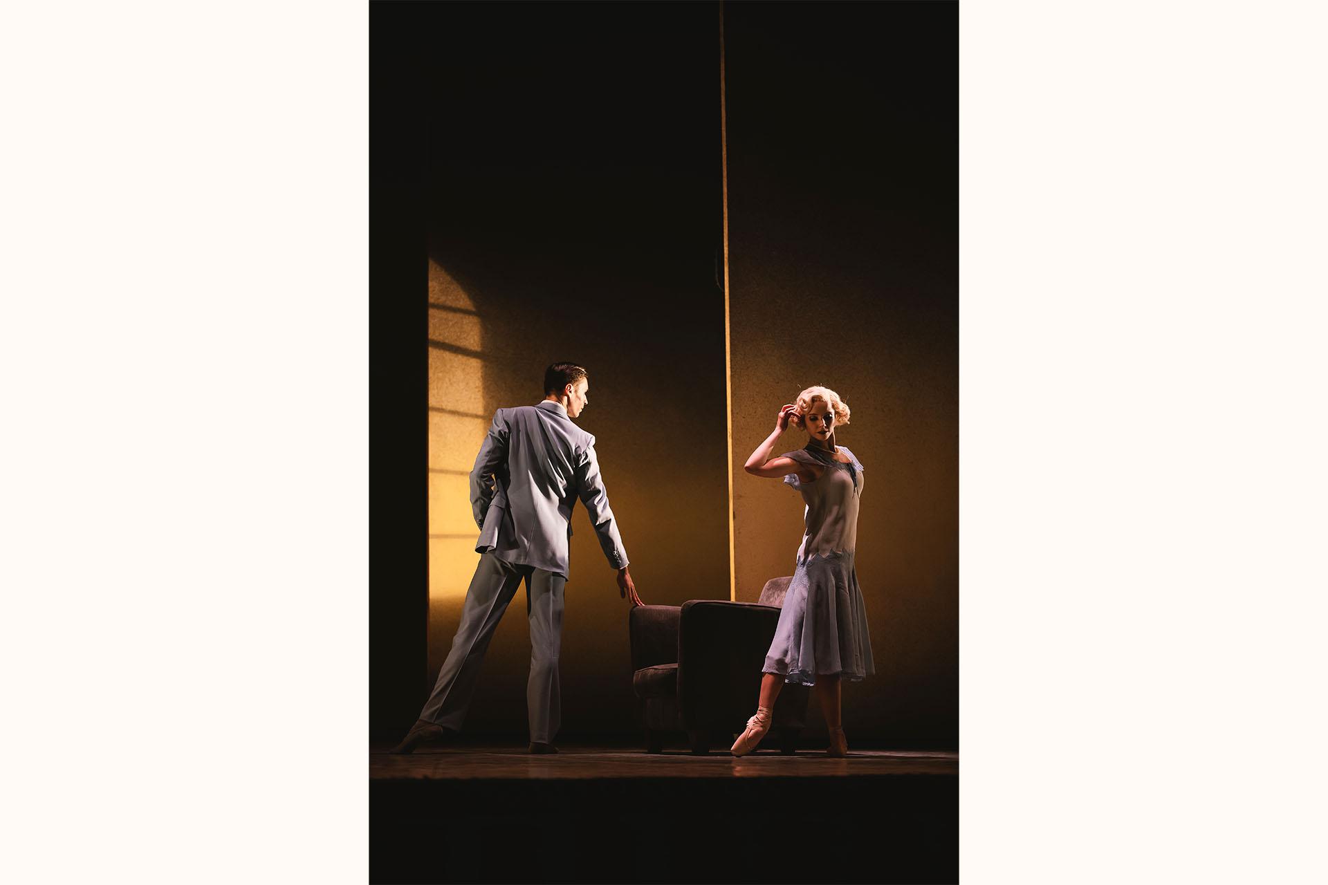 Male dancer in a pale blue suit looks angrily at a female dancer who is moving away from him