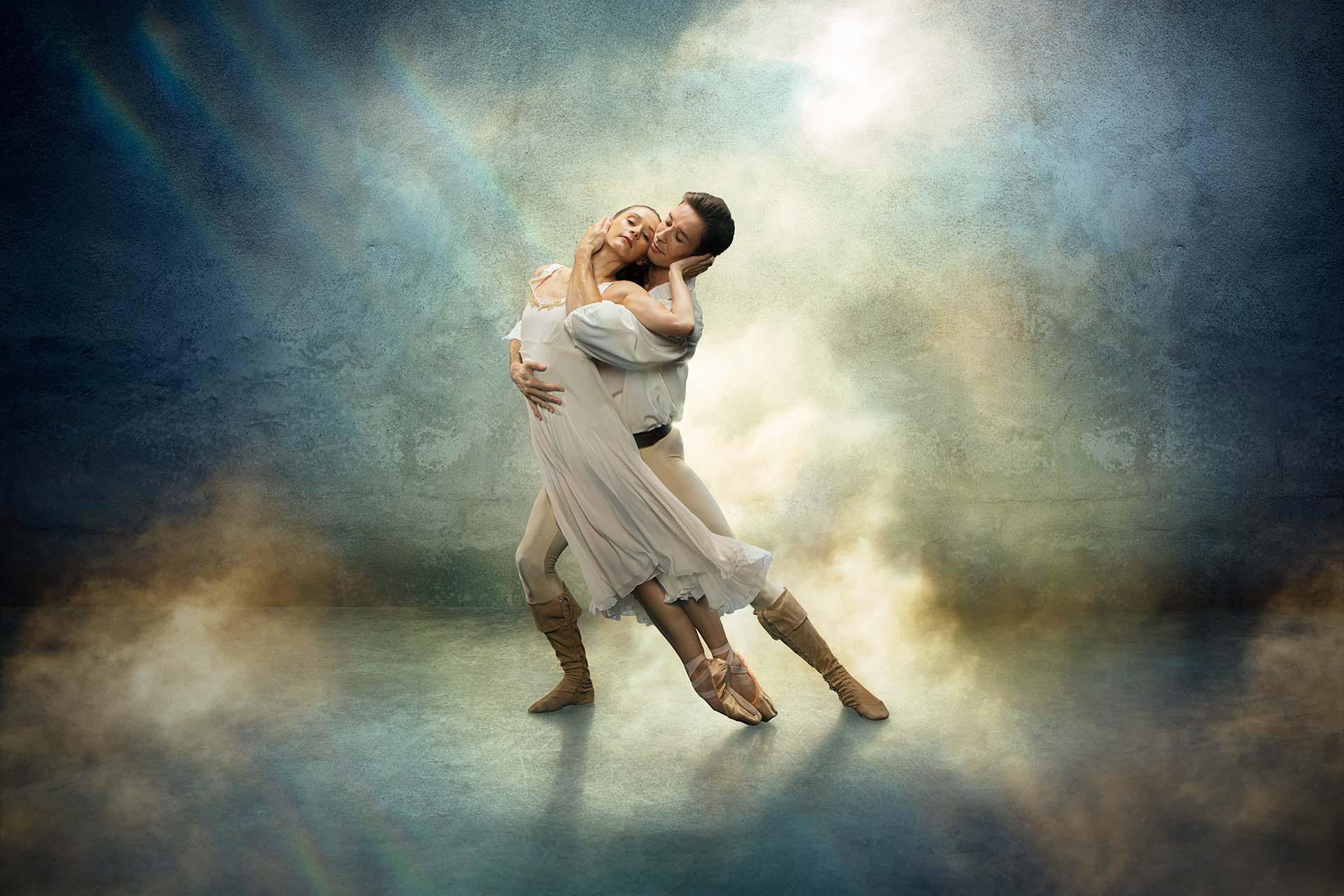 Star-crossed lovers Romeo & Juliet in a loving embrace, both wearing white against a fantasy blue and yellow background.