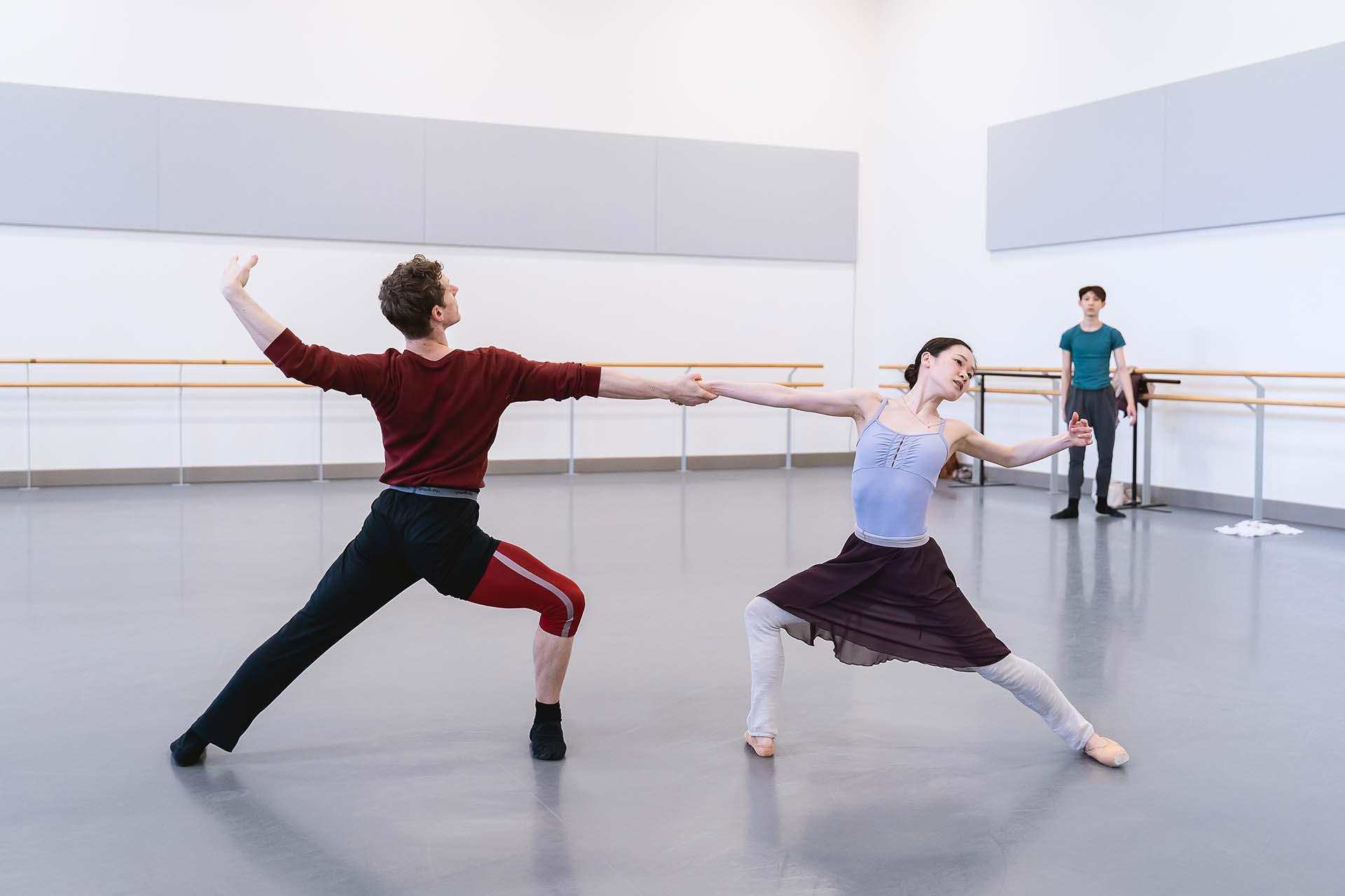 Two dancers, leaning and looking away from each other while holding their right hands
