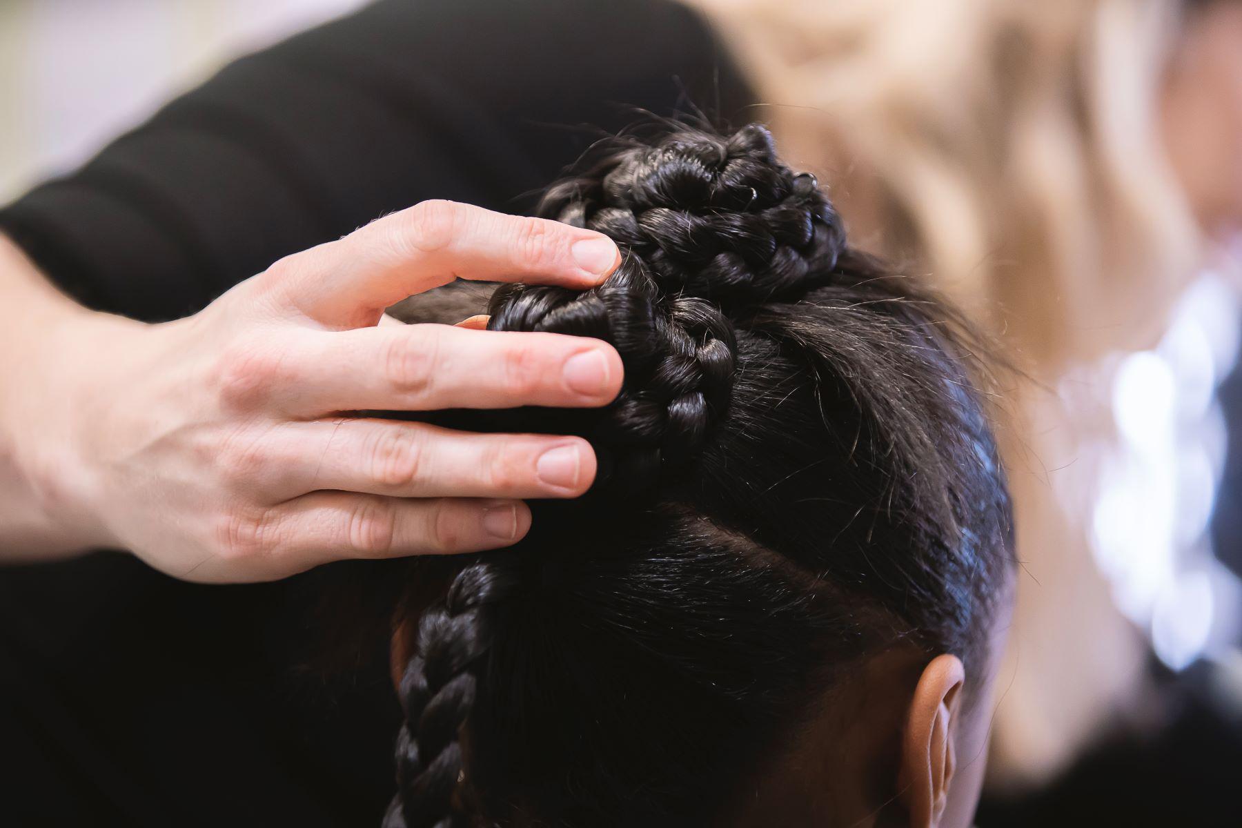A hand holds a braid on top of a dancers head.