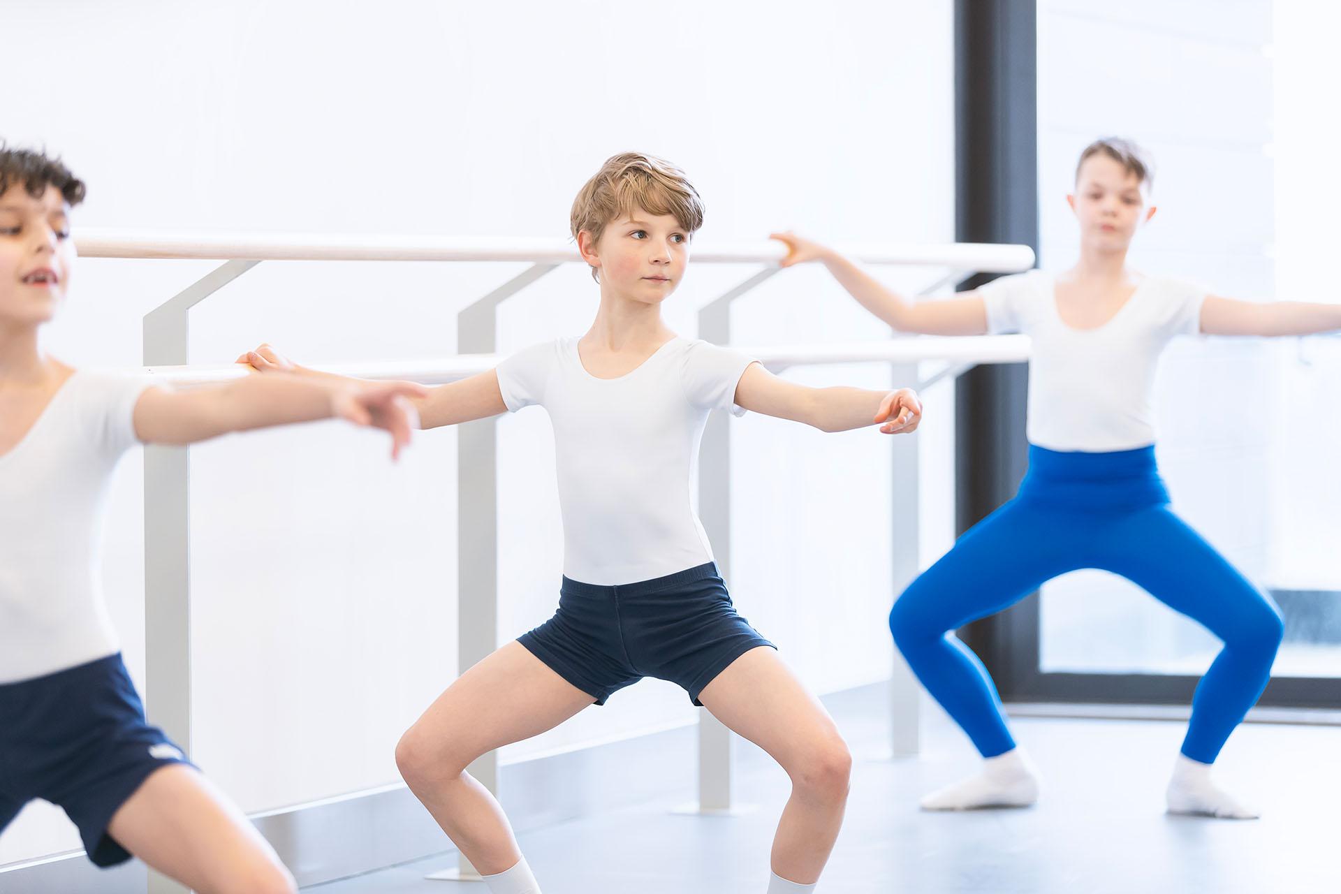 Boy at the barre, holding himself steady and his knees bent out.