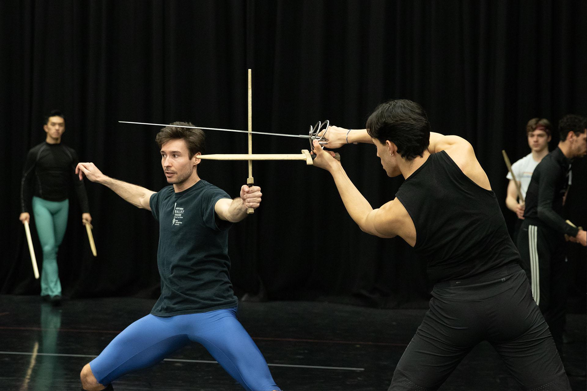 Recieving instruction on sword fighting in rehearsals the fighter in blue shorts blocks a double strike from his opponent in black trousers