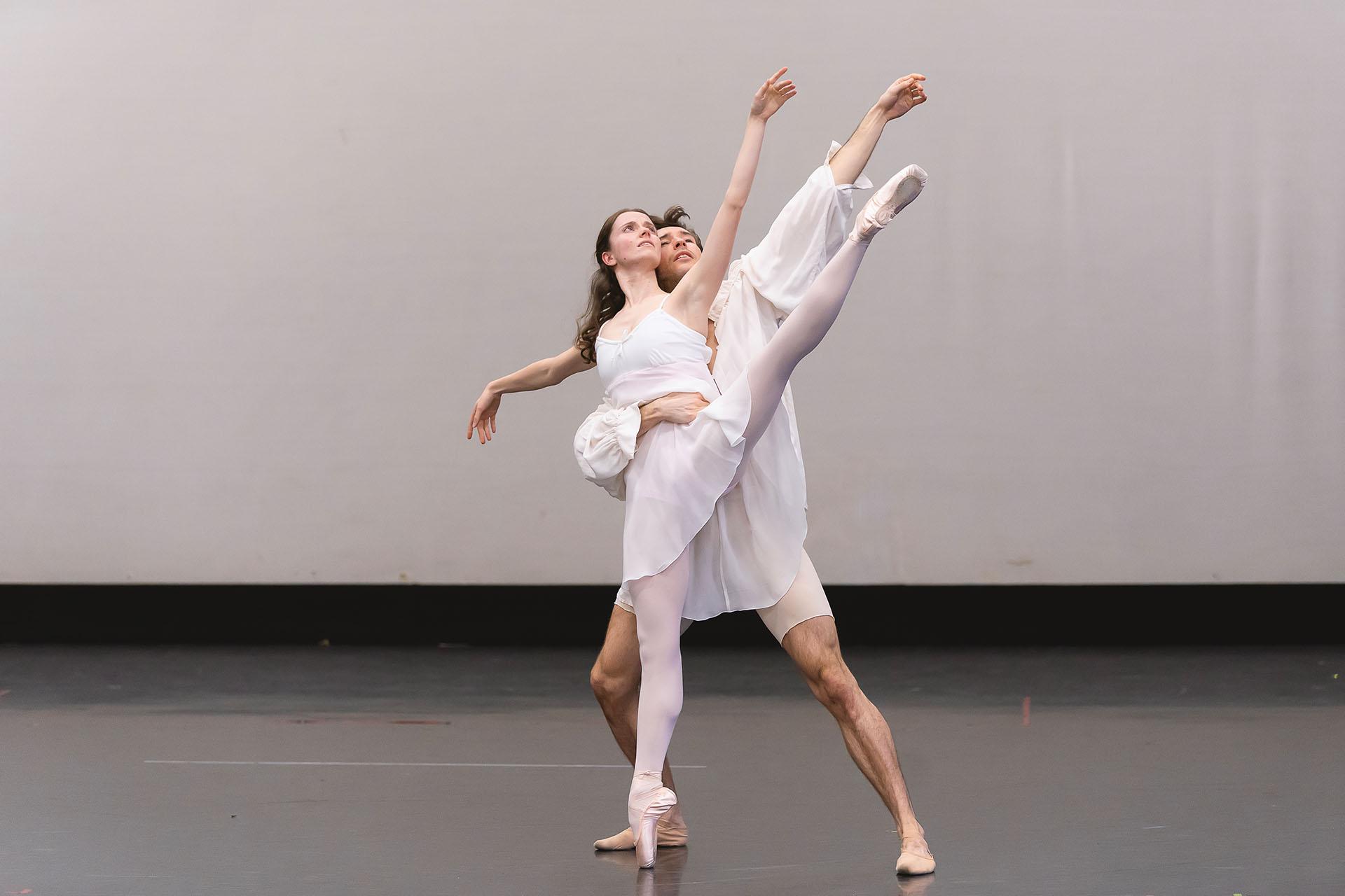 Dressed in white, two people dancing a duet, holding each other closely and with love.