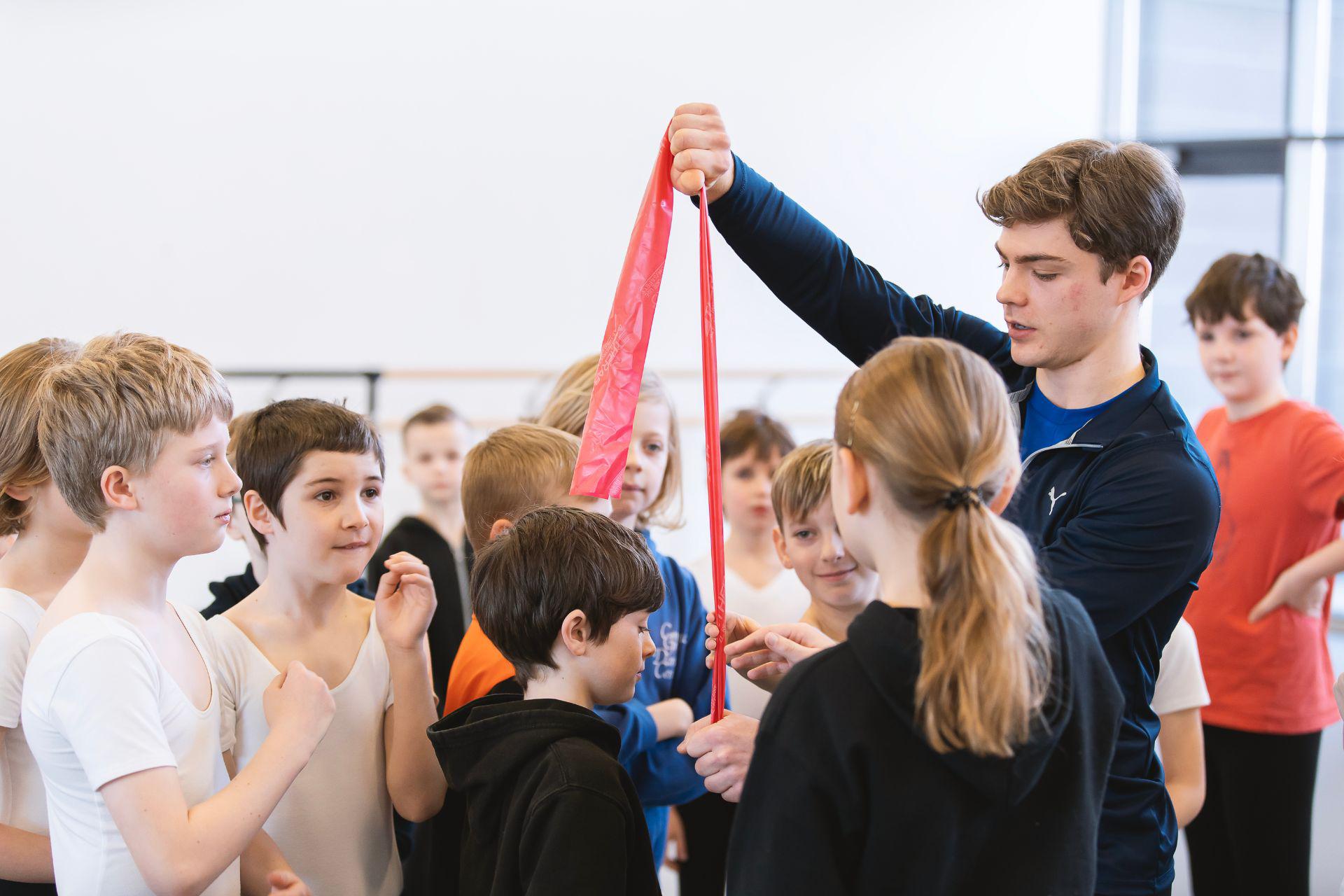 A dancer holds up a thin piece of fabric to a class of young boys