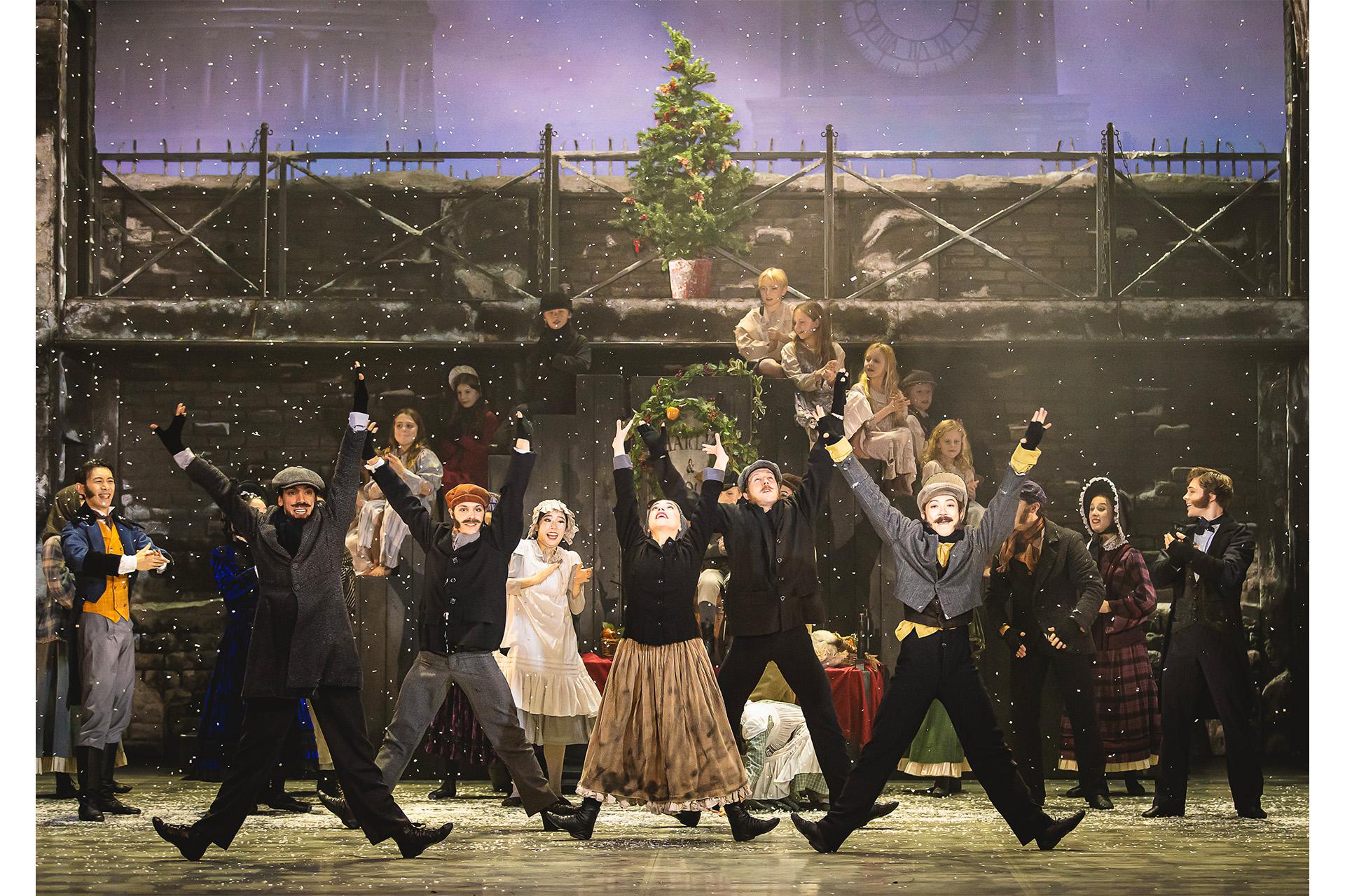 Townspeople dance with their arms in the air and legs spread apart as snow falls.