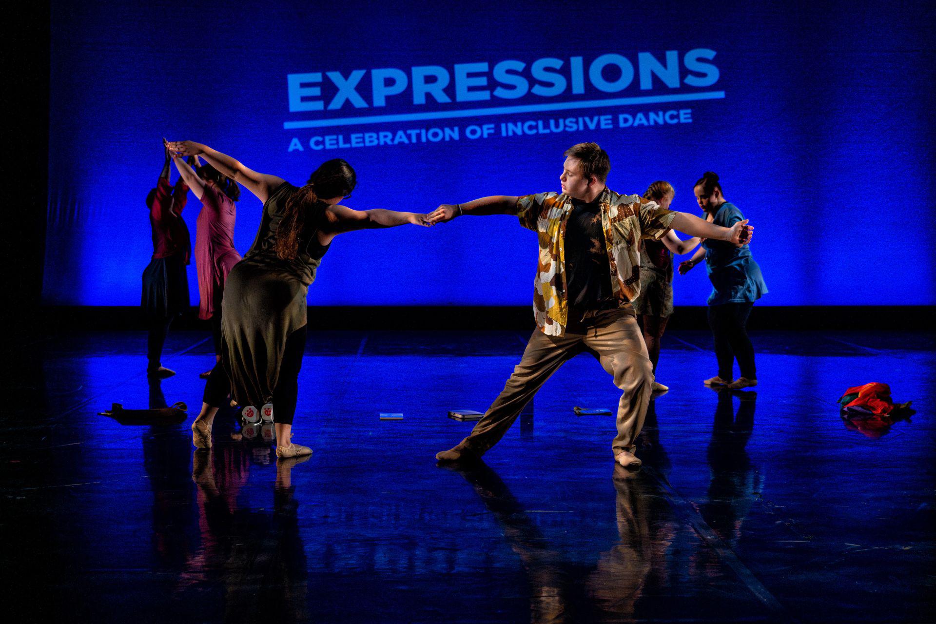 Dancers on a blue stage hold hands as they dance.