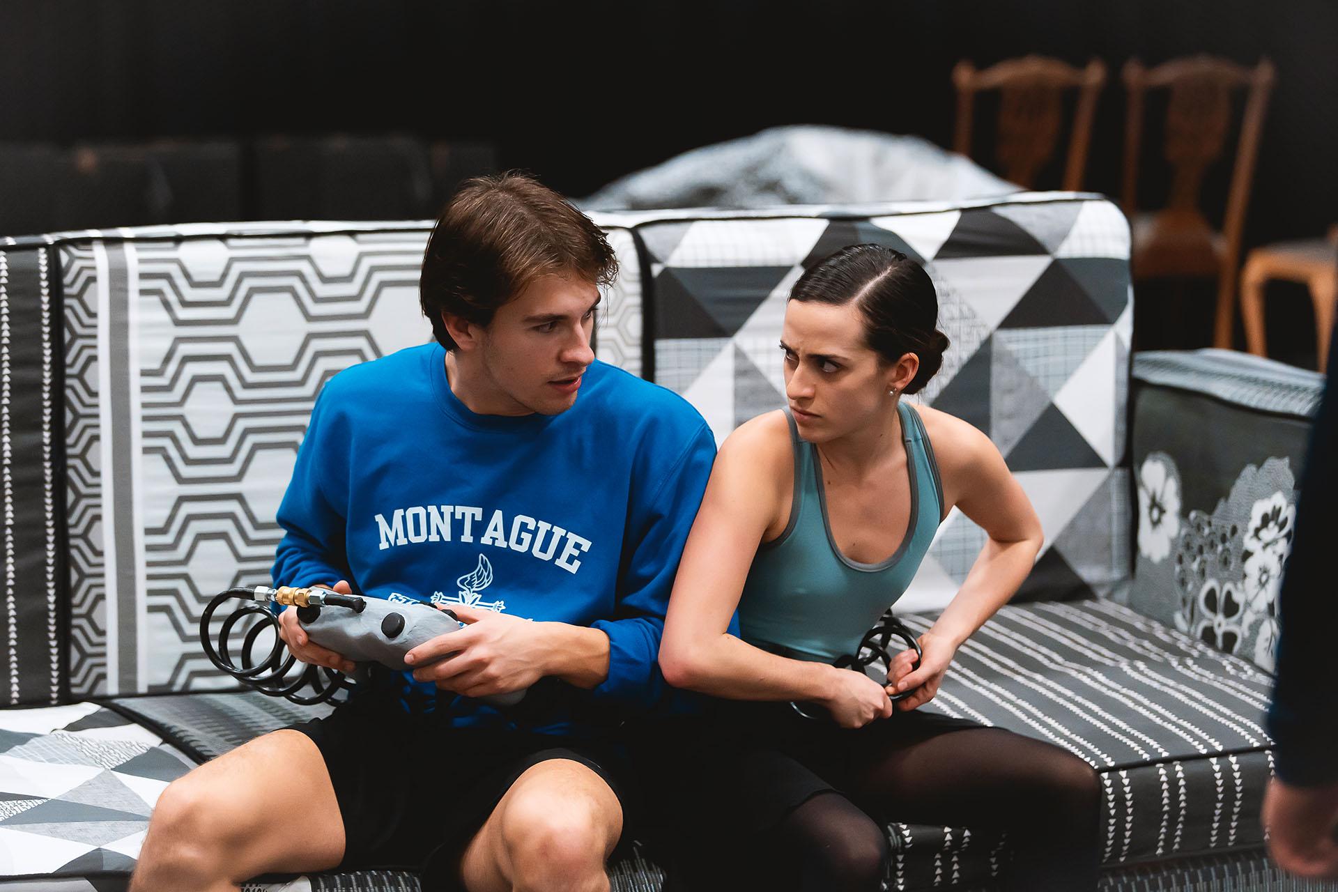 Two dancers acting petulantly facing each other while sat on a garish sofa