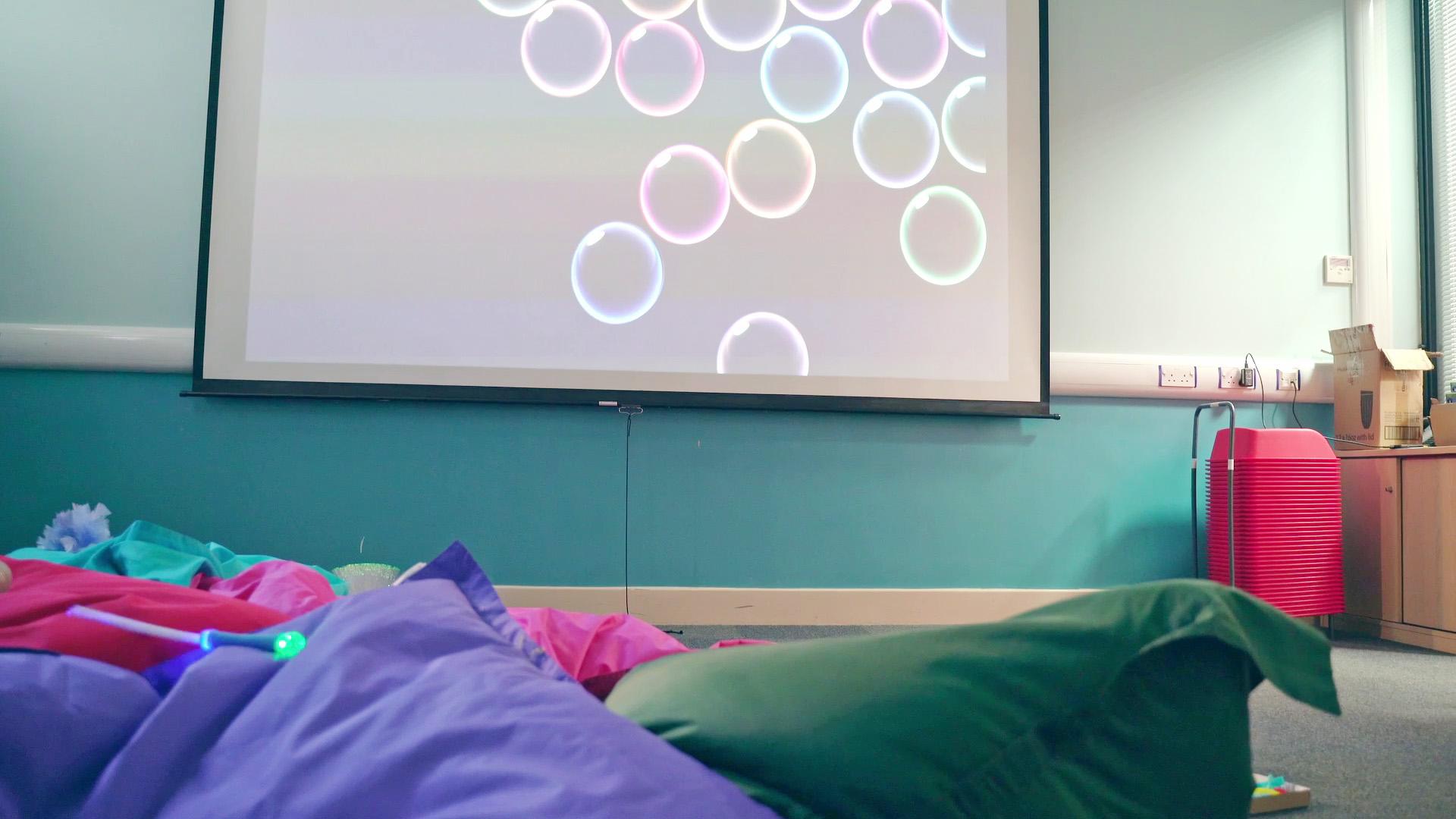 Large cushions on the floor and a relaxing animation projected onto the wall with lowered lighting and a quiet area