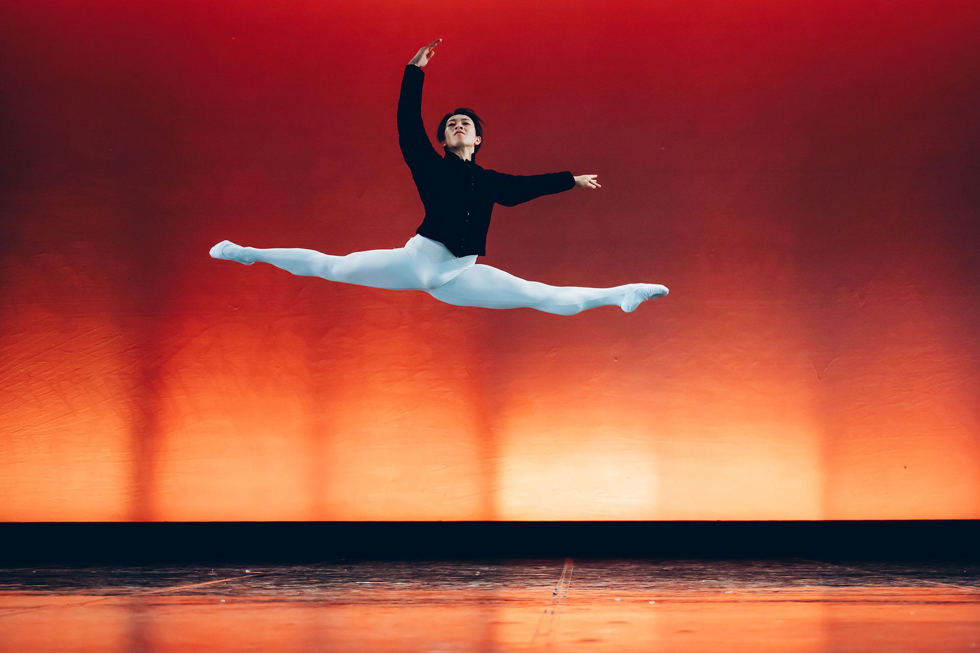 Male dancer leaps through the air grand jete, wearing white tights and a black top