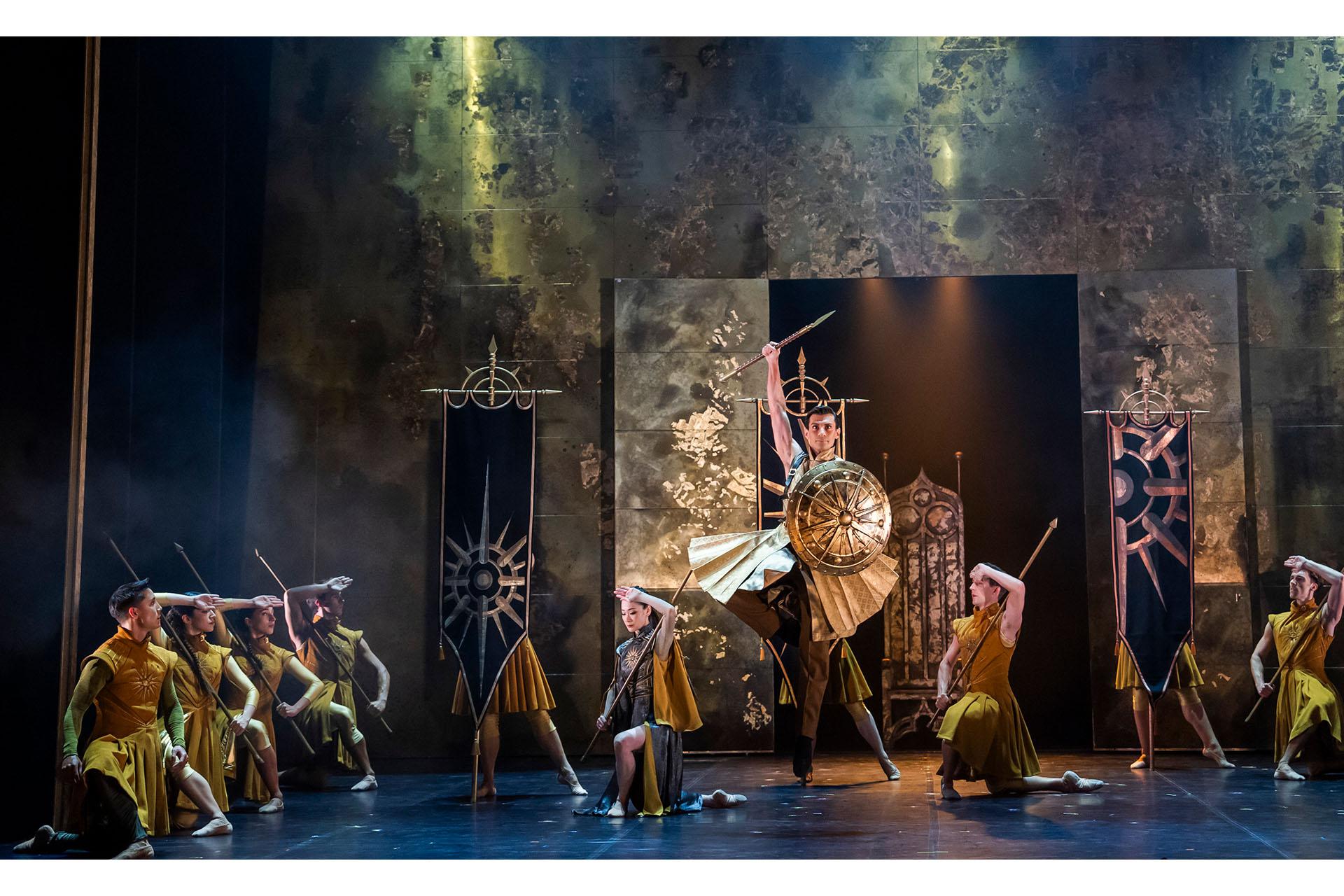 With his troops kneeling behind him, the king dances and leaps with his sword above his head and round shield on his arm.