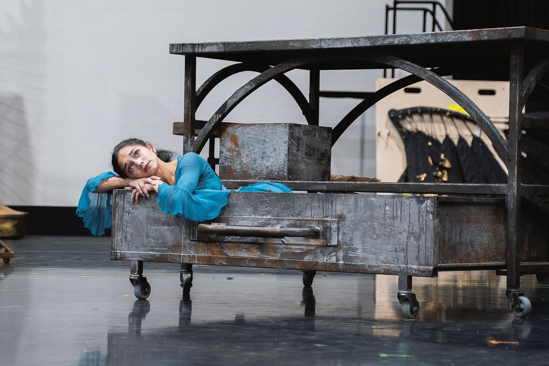 In an oversized drawer, a woman in blue leans over the edge and looks forlornly while resting her cheeks on her folded arms