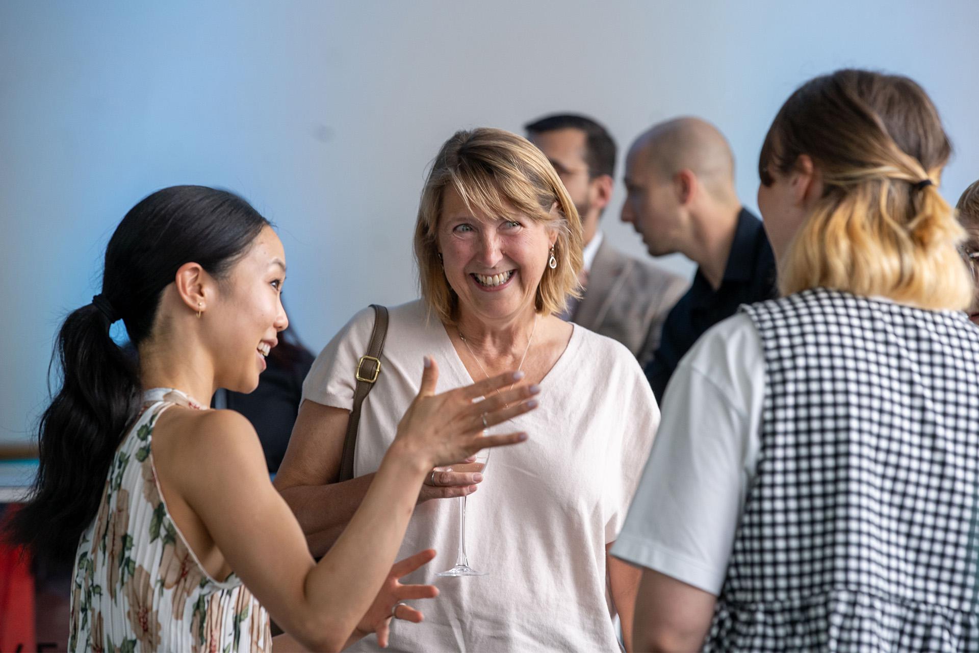 Woman with long dark hair tied back in a ponytail talked to a smiling woman in a white top