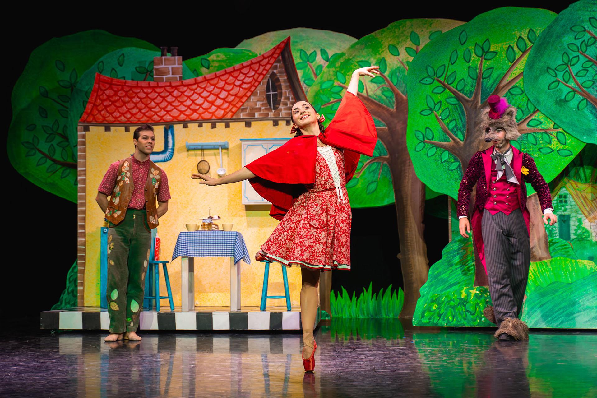 In front of her house and with her father and the wold looking on, Little Red in her bright red shawl and vibrant red pointe shoes dances and smiles