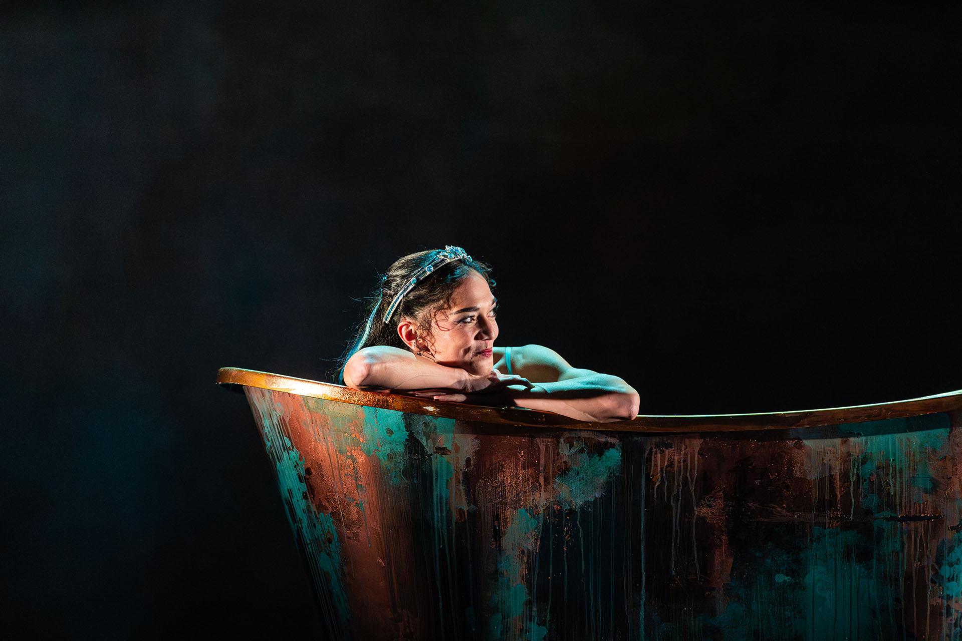 Ygraine leans on the edge of the copper bath and smiles