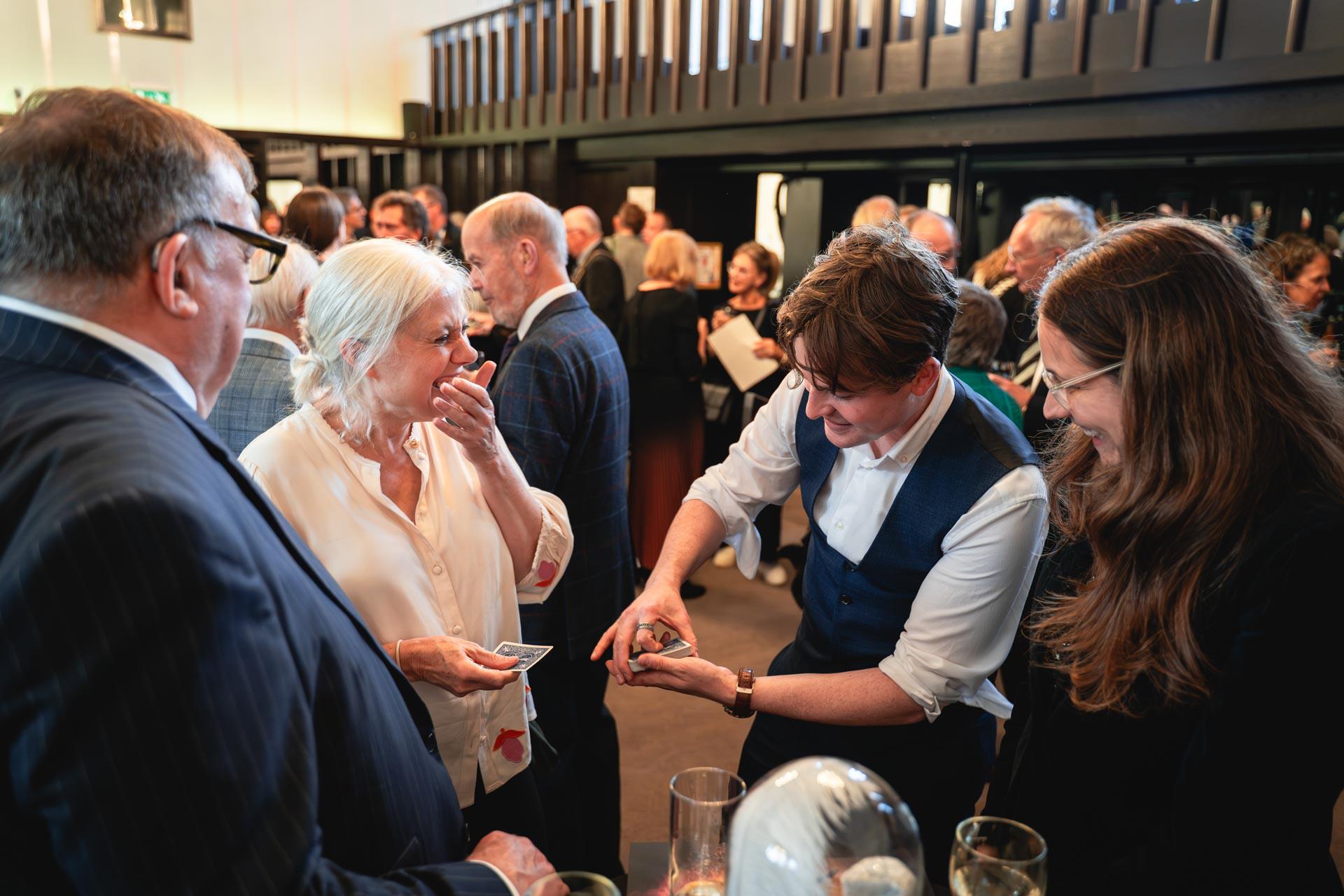 A magician dressed in a white shirt is performing a card trick to three people