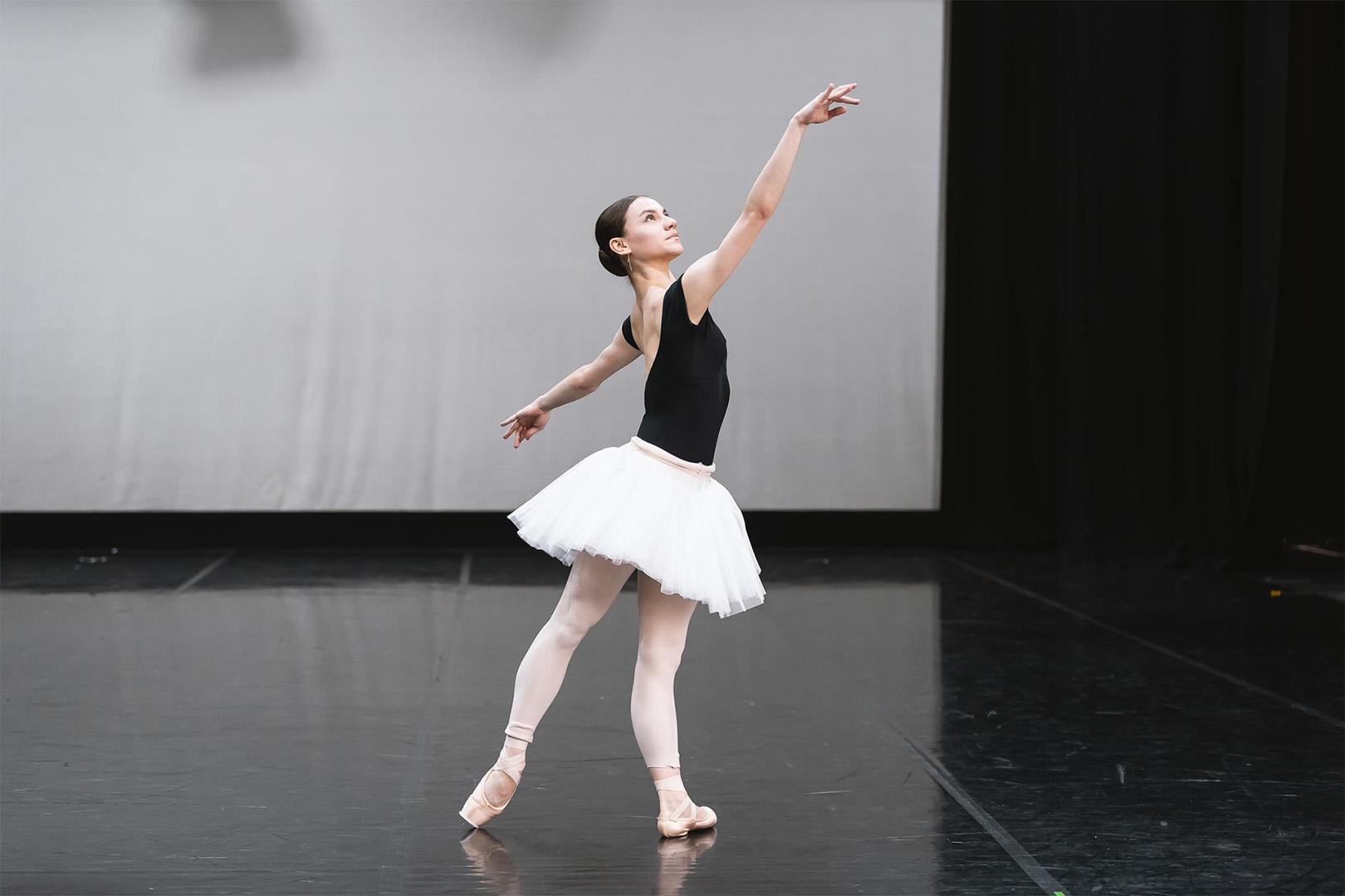 A dancer stood with one arm outstretched in a black leotard and a white tutu.