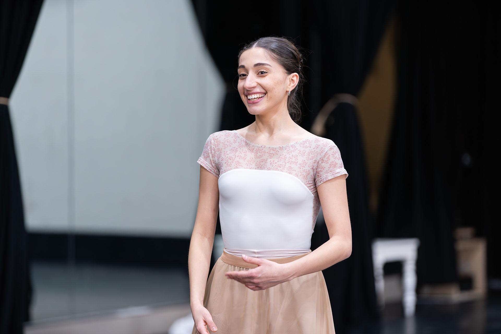 Dancer with broad smile, wearing white top in the rehearsal room