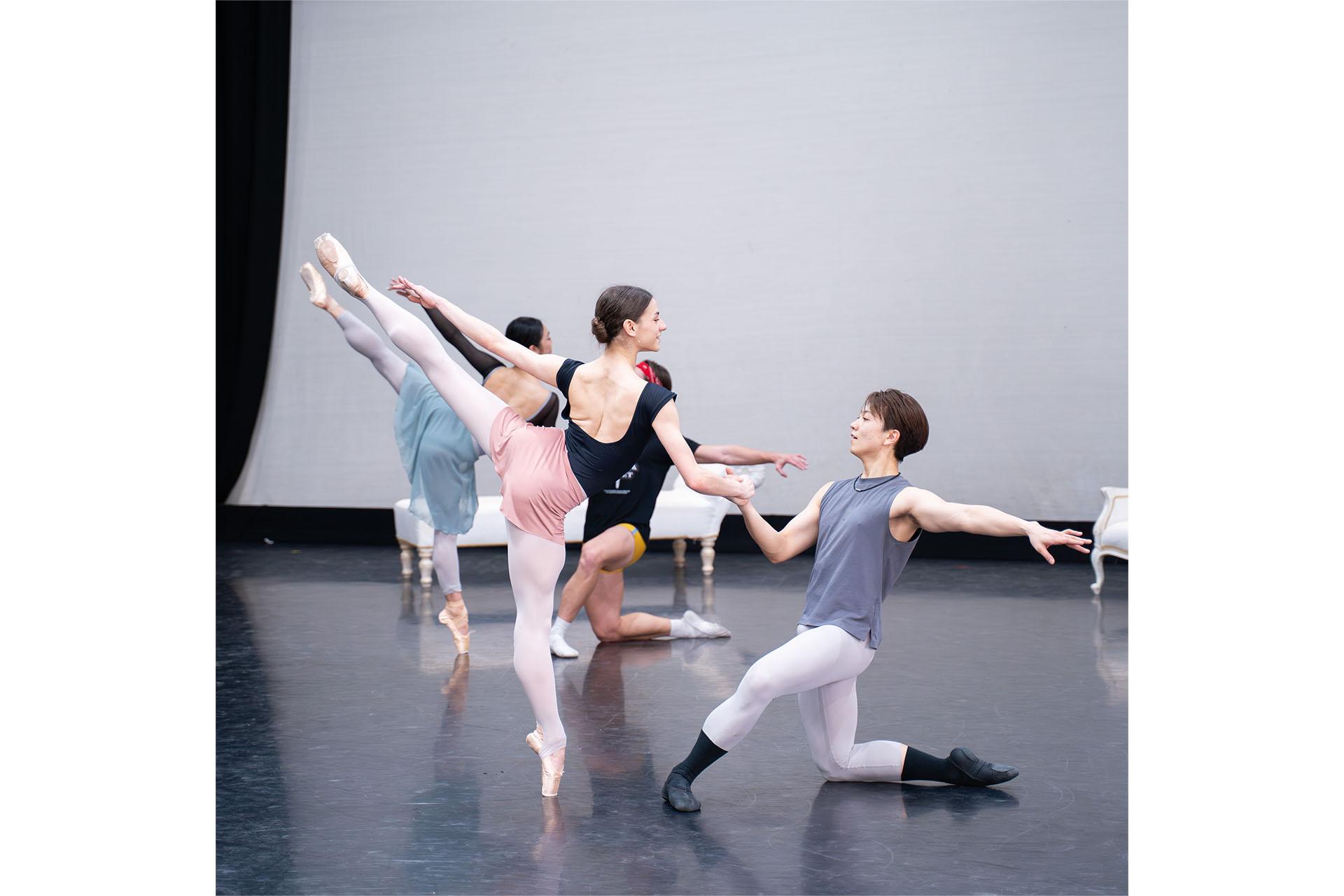 Couple in rehearsals, male dancer on one knee facing the woman, holding her hand supporting her balance as she stands on one foot, en pointe, leg raised high behind her