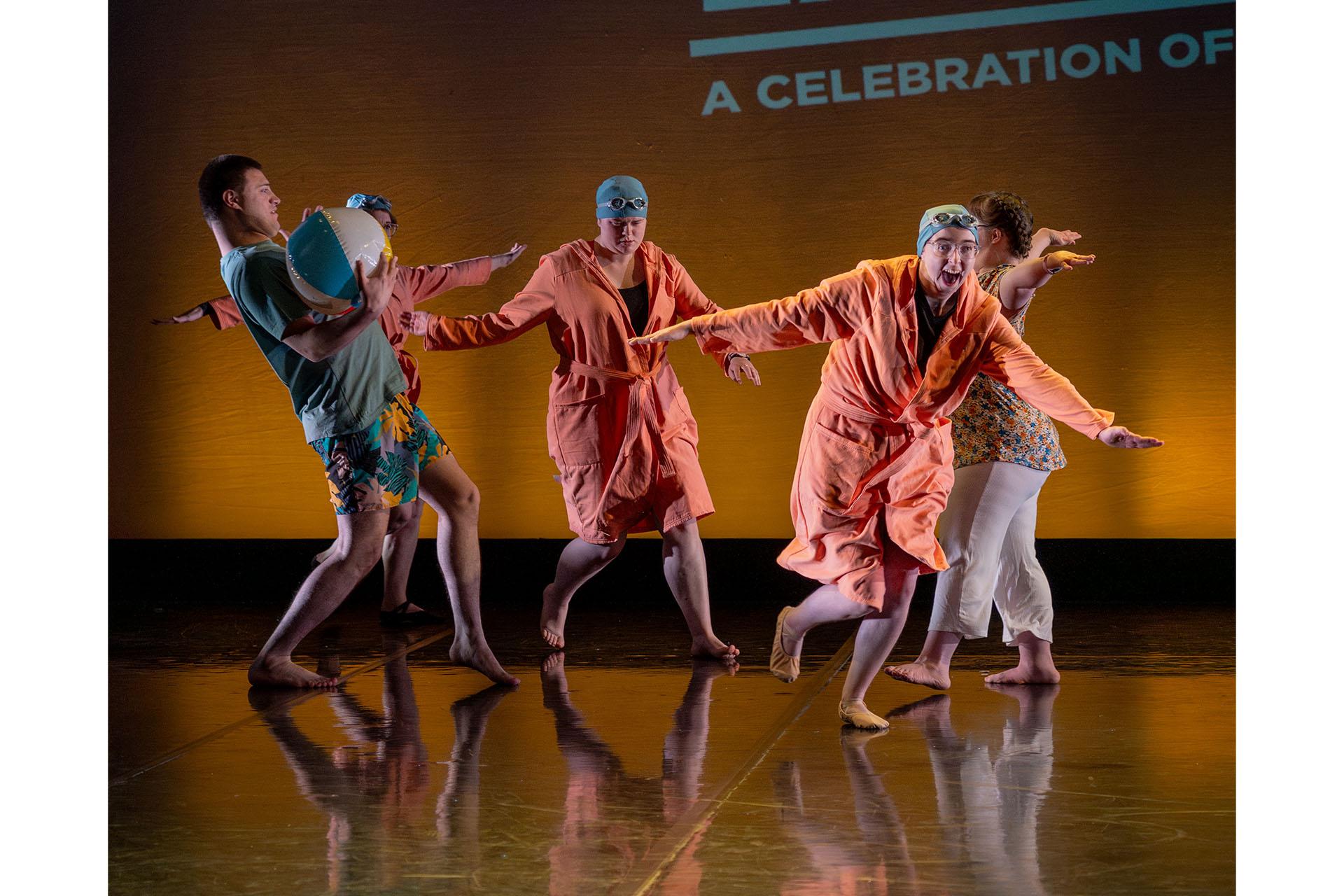 Five people on the dance stage filled with excitement, one with a beach ball, others wearing swimming caps